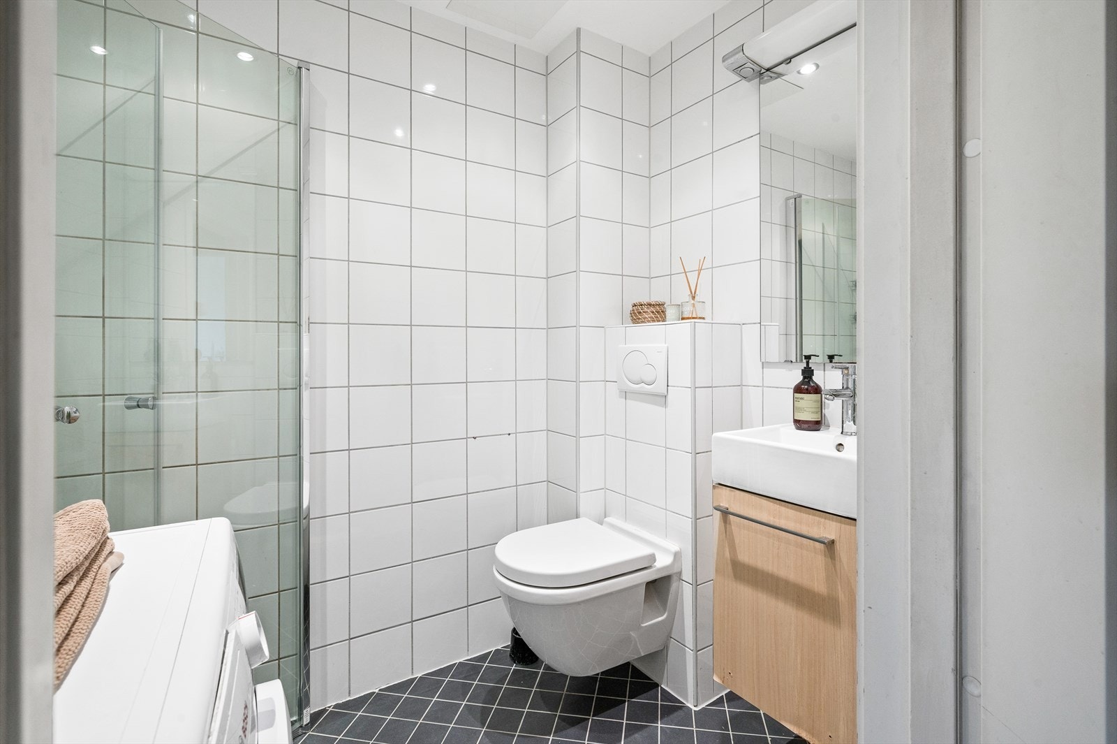 En velutnyttet baderomsløsning med flislagte overflater i en tidsnøytral utførelse. Opplegg for vaskemaskin og varmekabler i baderomsgulvet. Galleribilde