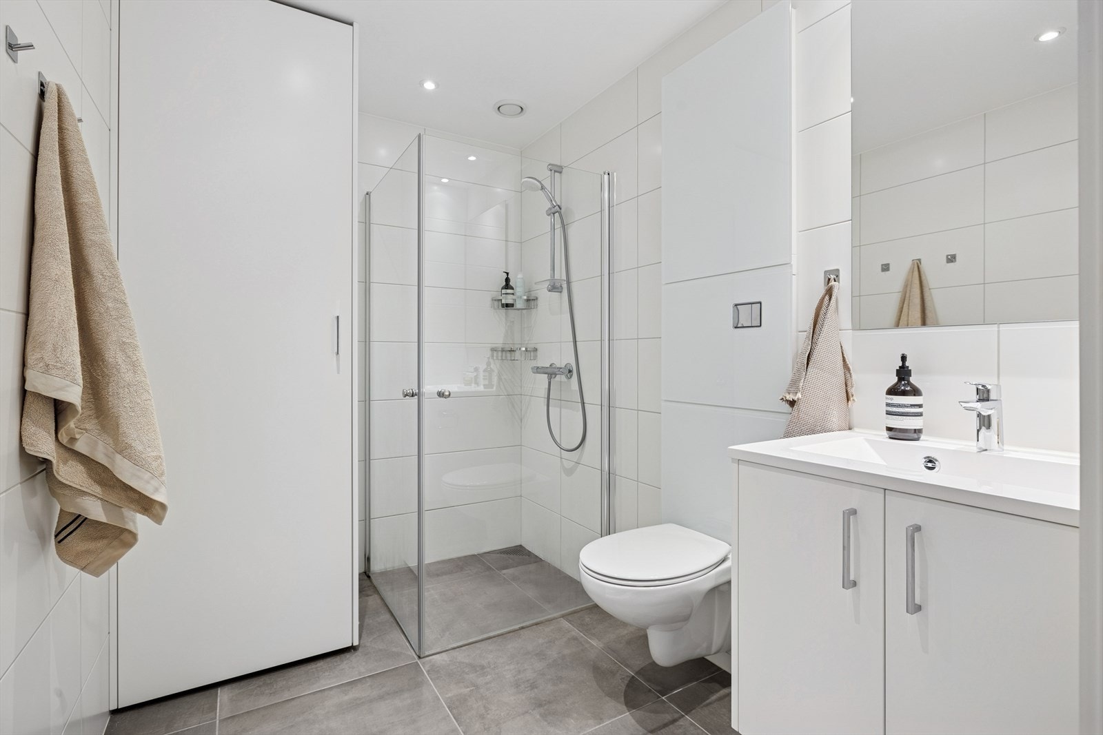 Flislagt baderom med vannbåren varme i gulvet, dusjhjørne, vegghengt toalett og opplegg til vaskemaskin/tørketrommel i skap Galleribilde