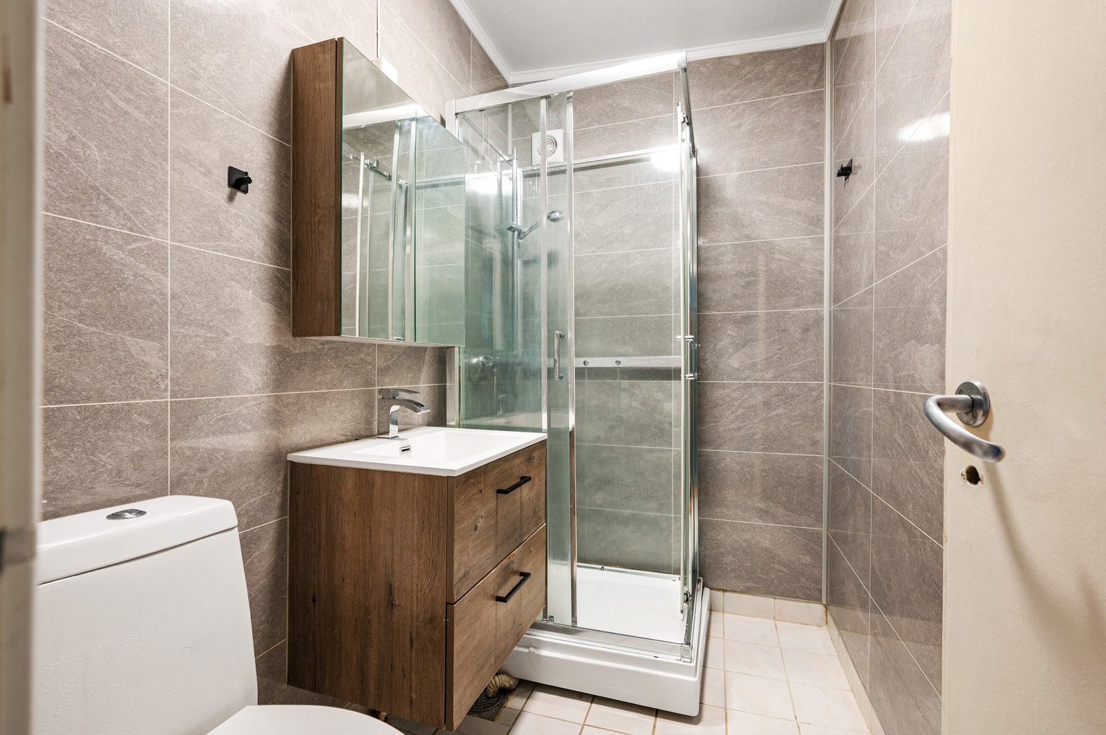 Badet er flislagt på gulv og vegger. Det er dusjkabinett og gulvstående toalett. Galleribilde