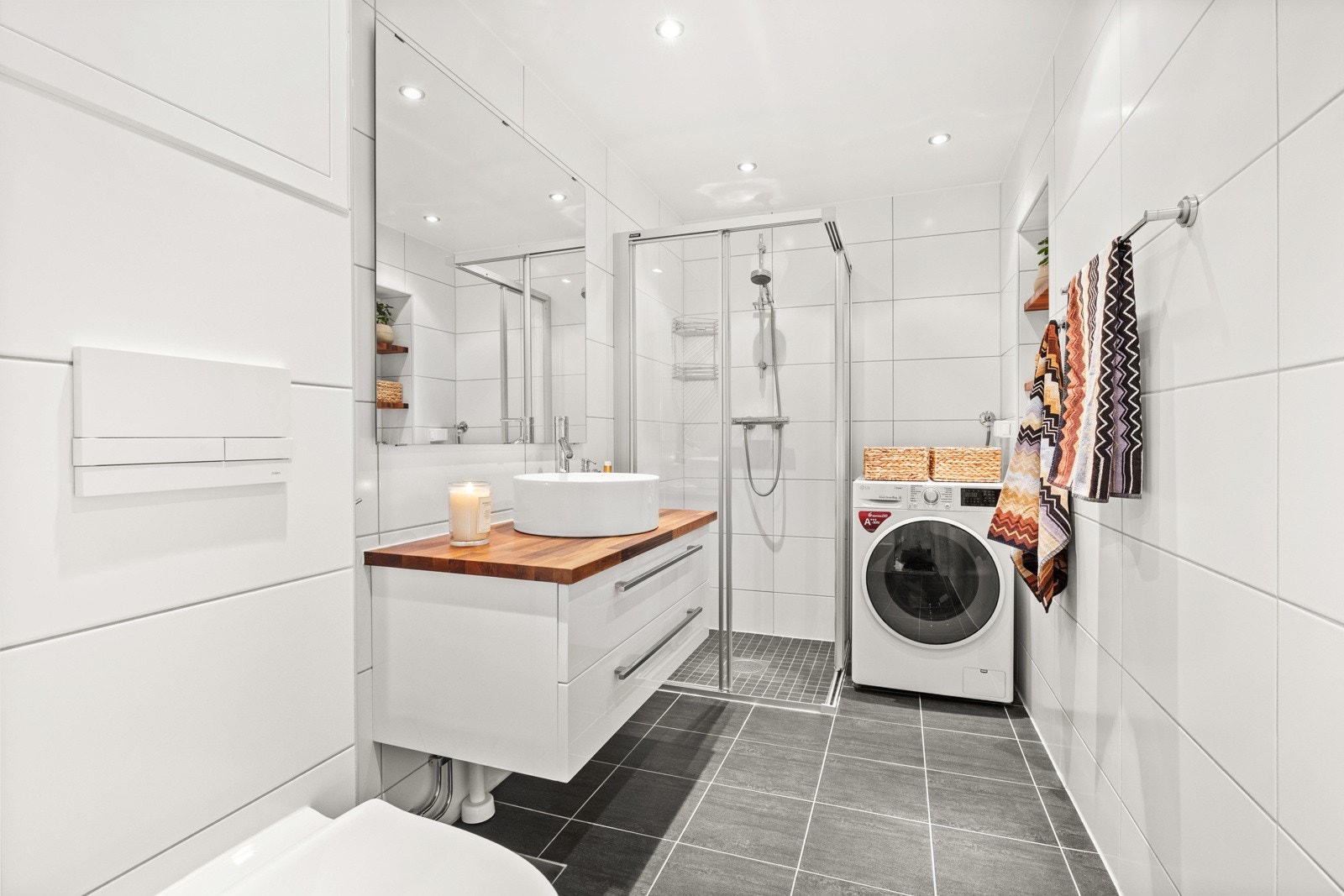 Baderom med vegghengt toalett med skjult sisterne, servant på heltre benkeplate og dusjhjørne i glass med aluminiumsprofiler. Galleribilde