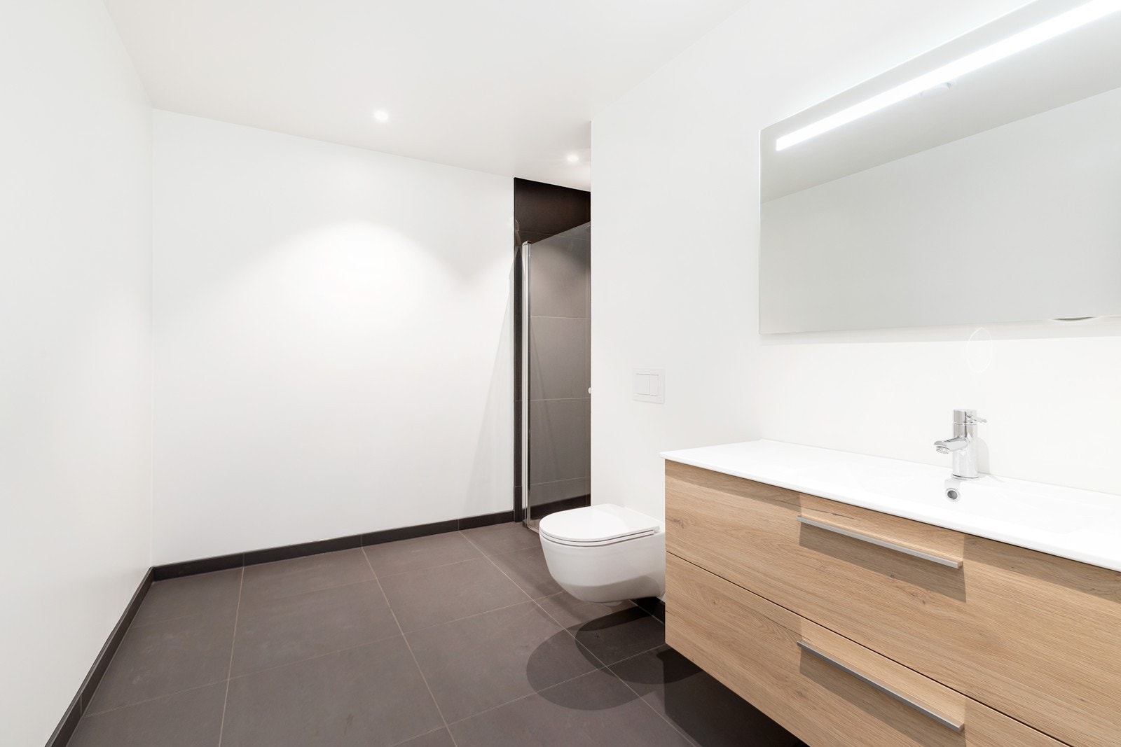 Lekkert og delvis flislagt baderom med vegghengt toalett, dusjhjørne og servant. Det er downlights i himling. Vis a vis baderommet er det et praktisk vaskerom/ teknisk rom. Galleribilde