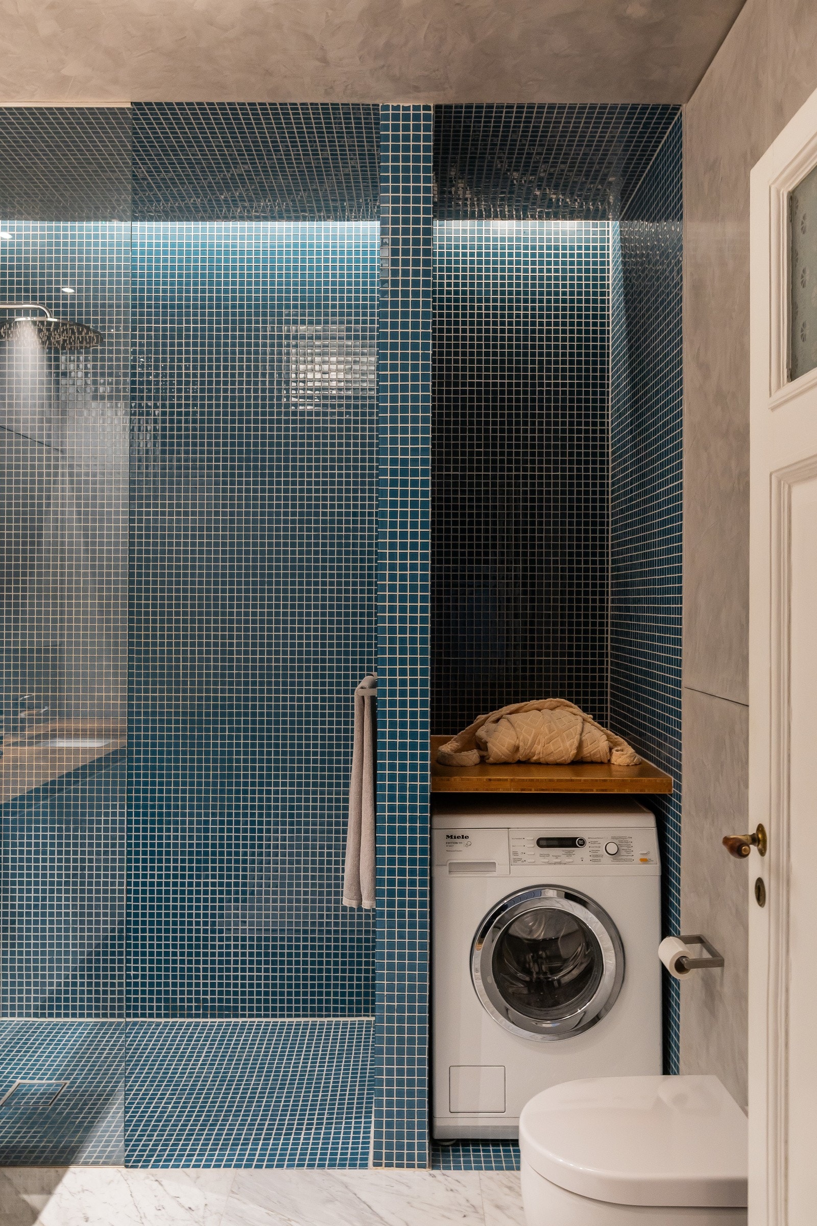 Rommet har en stor dusjnisje i glassmosaikk med glassvegg og regnfallsdusj. Servantskap med underlimt servant på bambus-benkeplate. Veggmontert toalett. Opplegg til vaskemaskin i hjørnet med benkeplate for praktisk boltreplass/arbeidsbenk. Galleribilde