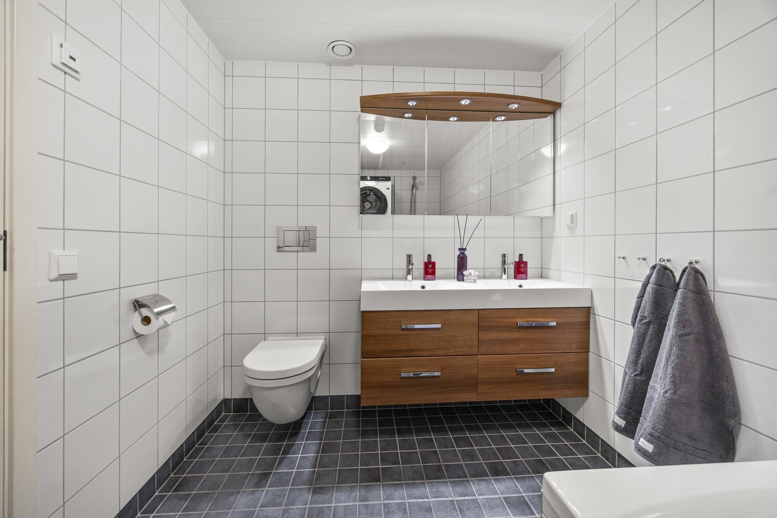 Baderomsinnredningen har mørke, finerte fronter og består av en heldekkende dobbelservant på en skuffeseksjon og et bredt speilskap med belysning Galleribilde