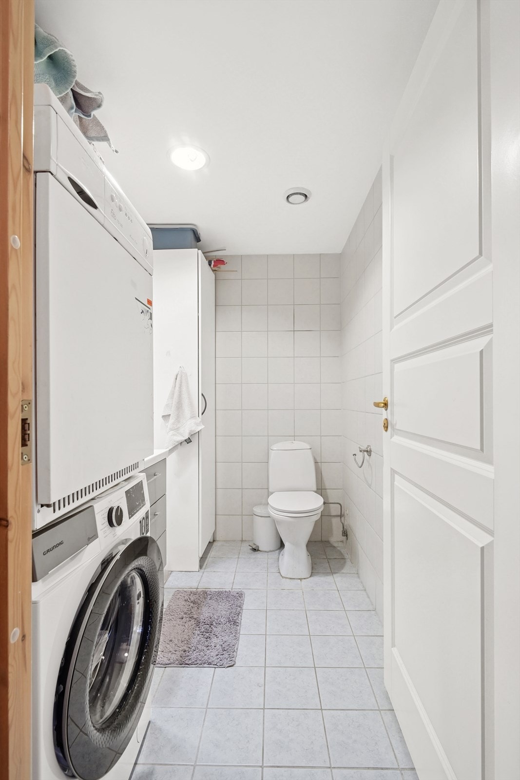 Flislagt kombinert WC og vaskerom, innredet med toalett, servant, samt opplegg for både vaskemaskin og tørketrommel. Galleribilde