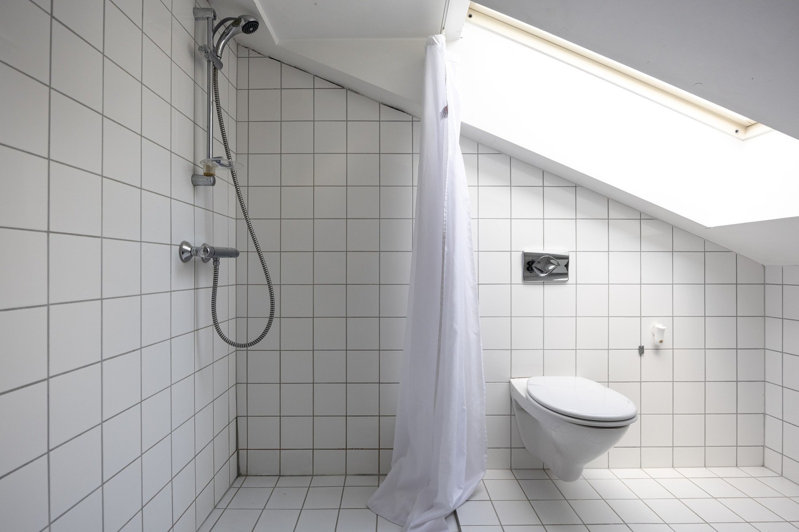Badet har hvite fliser på gulv og vegger, varmekabler i gulv, downlights og overlys fra takvindu. Galleribilde