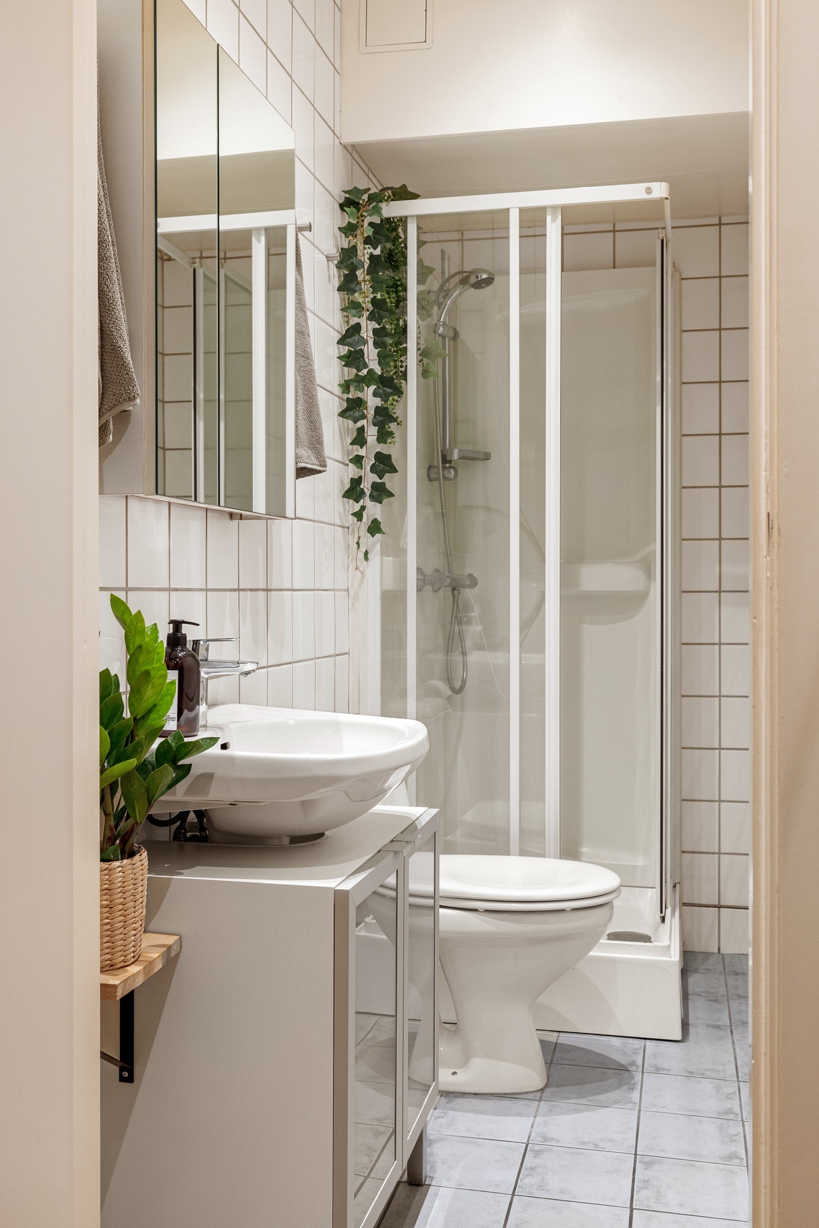 Flislagt baderom med dusjkabinett med skyvedører, vegghengt servant og innredning med dører. Galleribilde