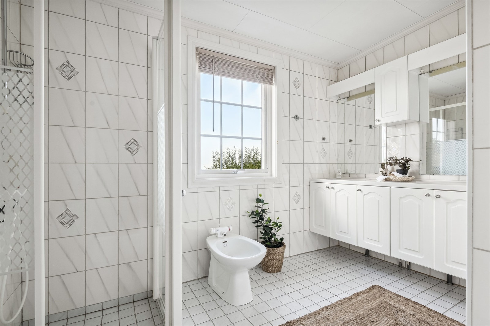 Bad 1.etasje er flislagt med varme i gulv. Badet er utstyrt med en vegghengt dobbel servant med underskap, dusjvegger og bidé. Galleribilde