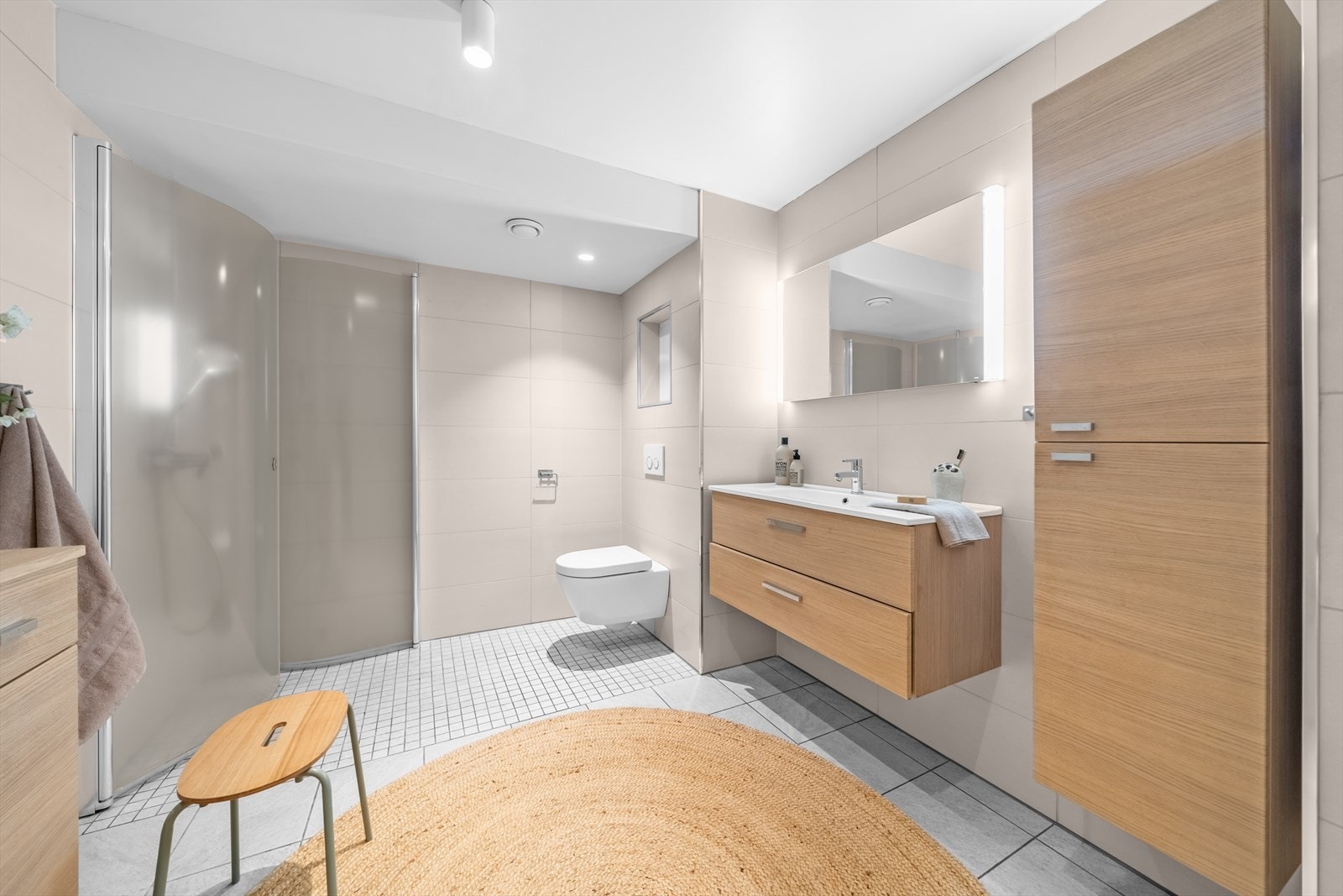 Badet er innredet med en dusjsone med innfellbare glassdører, vegghengt toalett, opplegg for vaskemaskin, servant og tilhørende skapplass. God belysning og pene fliser gir badet et moderne og stilrent inntrykk. Galleribilde