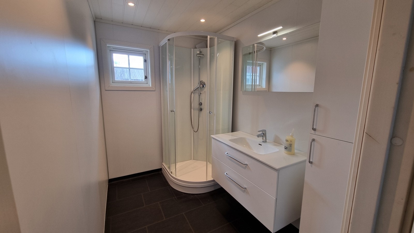 Bad med nyere innredning med dusjkabinett, servant med skuffer og høyskap. Galleribilde