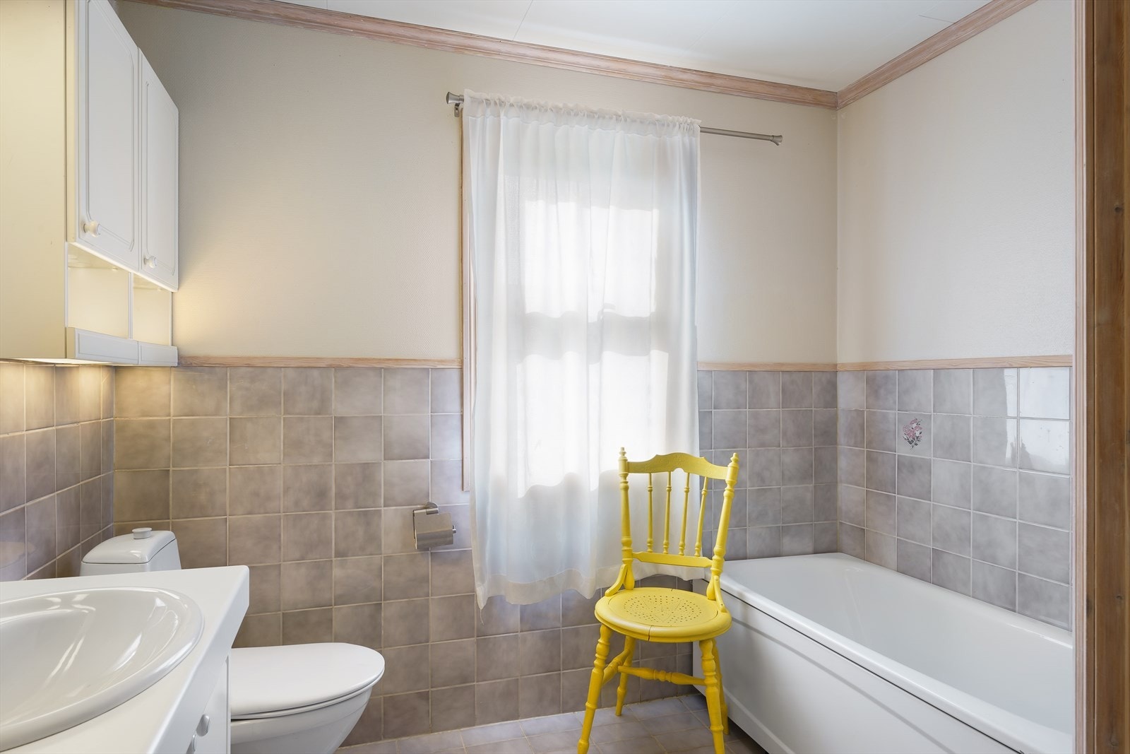 Den eldre delen av badet har badekar. Badet er innredet med dusjnisje med glassvegger, hvit profilert baderomsinnredning med nedfelt servant, høyskap, speil og belysning, badekar og gulvmontert toalett. Galleribilde