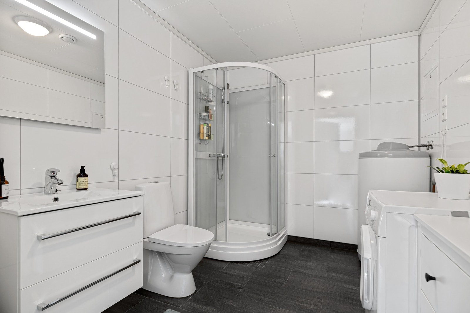 Pent bad med flislagt gulv med varmekabler, plater på vegger og dusjkabinett montert Galleribilde