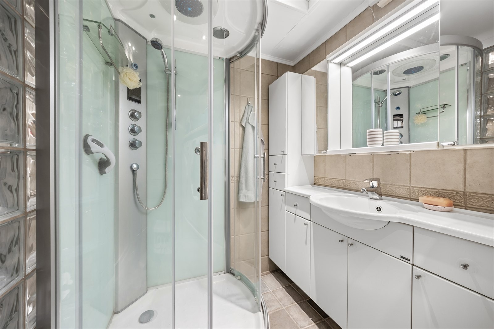 Badet er utstyrt med servant med underskap, speil, dusjkabinett og toalett Galleribilde