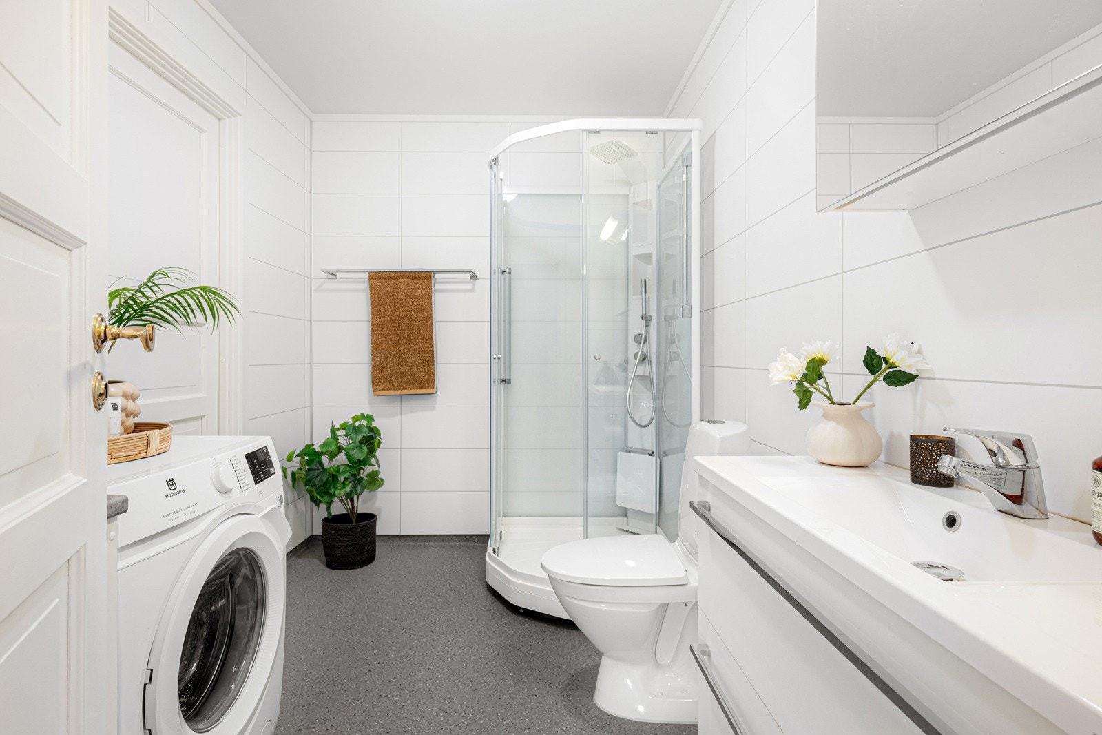 Lyst og fint bad med hvit baderomsinnredning, dusjkabinett og opplegg for vaskemaskin og tørketrommel Galleribilde