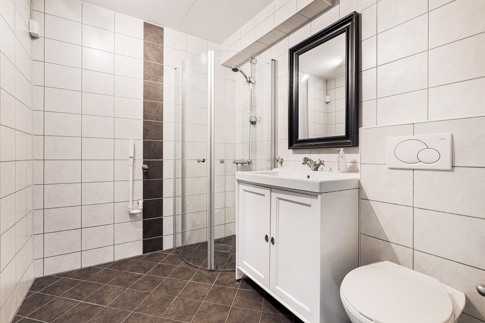 Badet er pent helfliset og inneholder servant i møblement, vegghengt toalett og dusjhjørne med dører i klart glass. Galleribilde