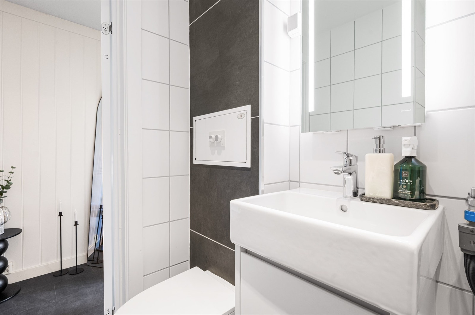 Innredningen består blant annet av gulvstående skapinnredning med ovenpåliggende servant. Speil med belysning og stikkontakt på vegg over servanten. Videre har badet dusjhjørne med innfellbare dører av glass og vegghengt toalett. Galleribilde