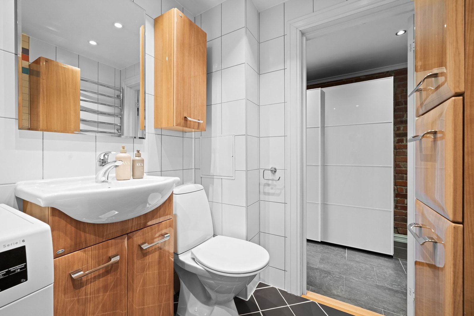 Videre har badet et toalett, opplegg for vaskemaskin og et dusjhjørne med innfellbare glassdører Galleribilde