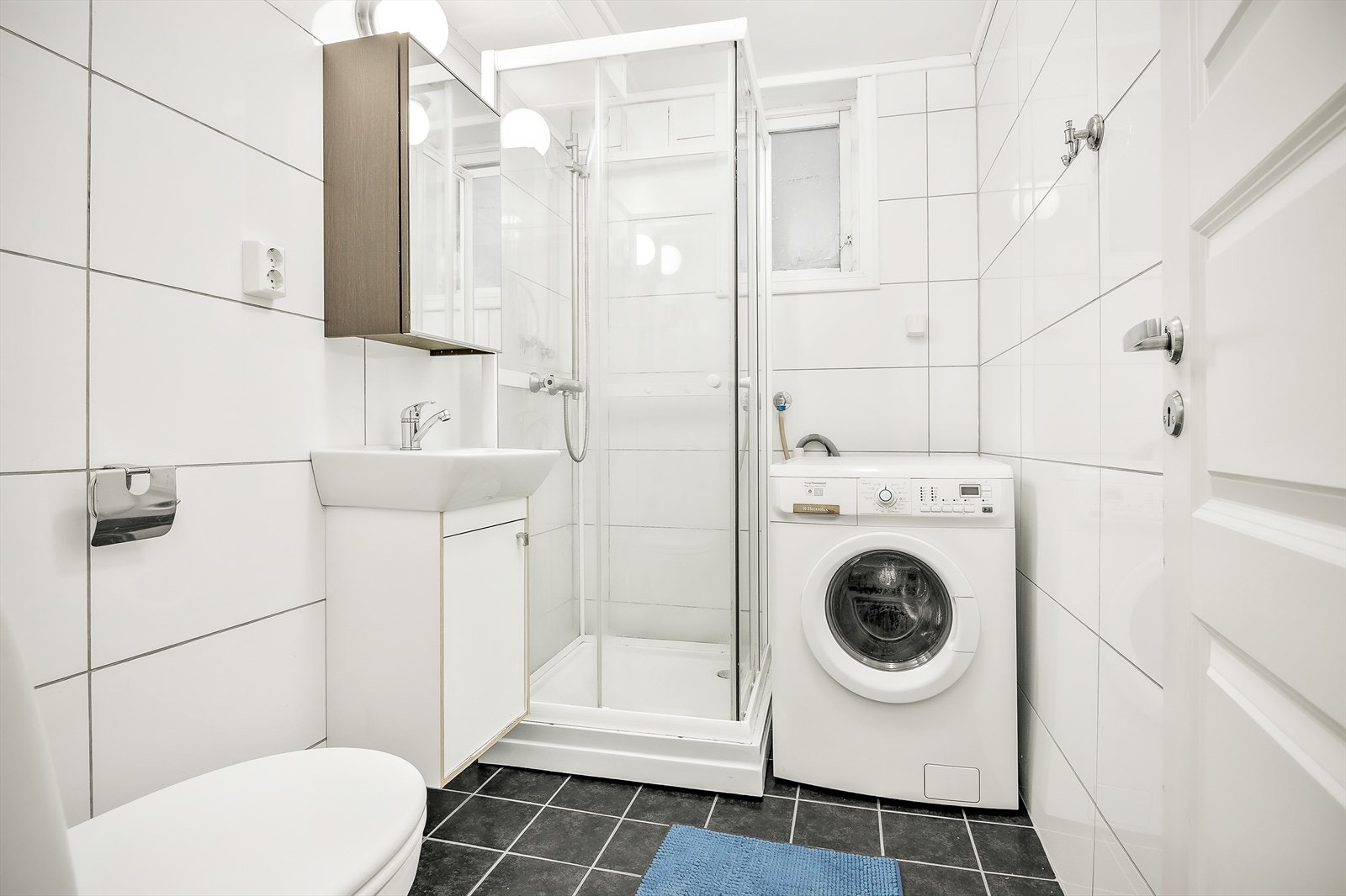 Flislagt bad fra ca. 2016/2017 med innredning bestående av klosett, dusjkabinett og baderomsinnredning med speilskap. Badet har opplegg for vaskemaskin og tørketrommel Galleribilde