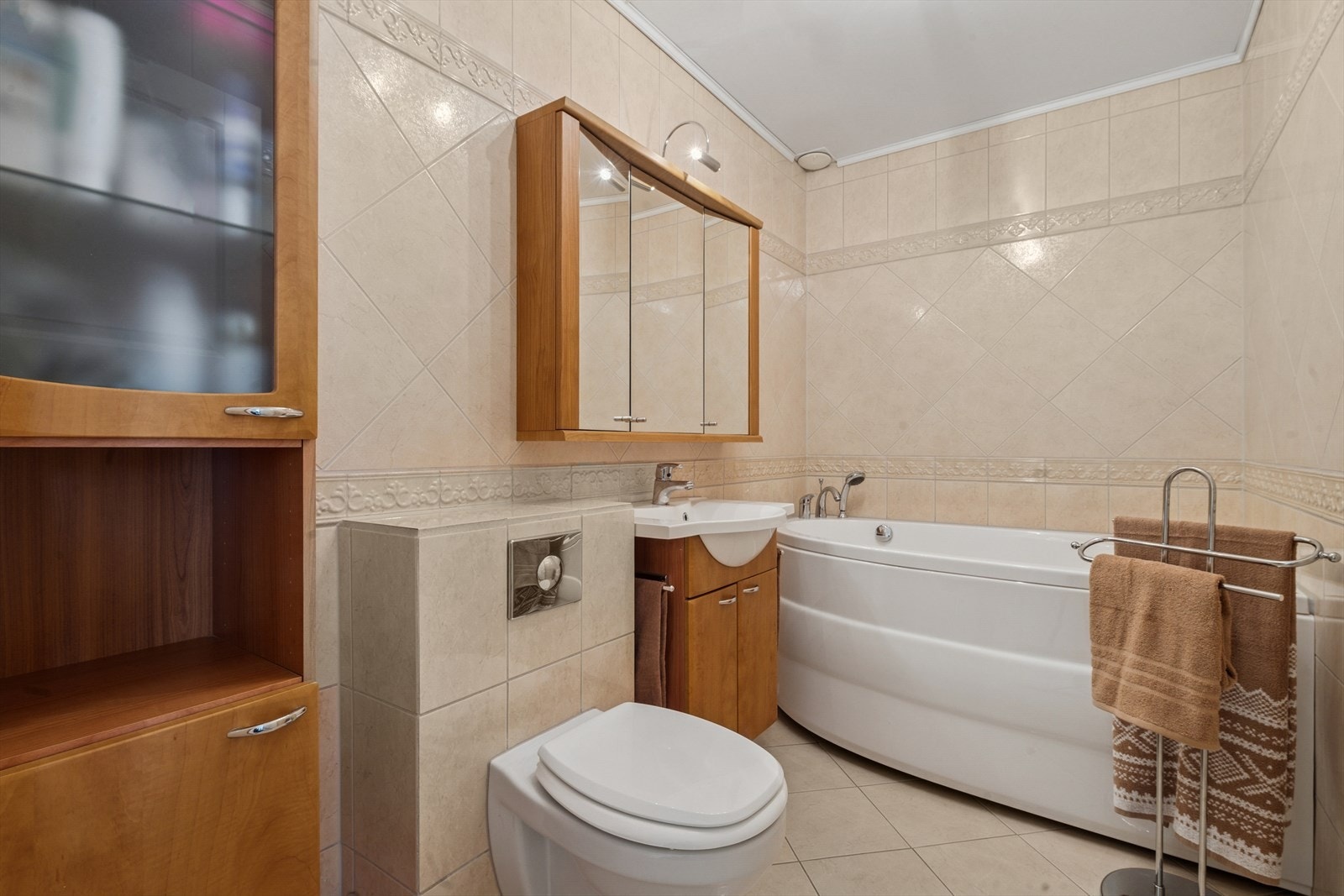 Helfliset baderom innredet med vegghengt toalett, badekar og møblement med servant, speil og belysning. Galleribilde