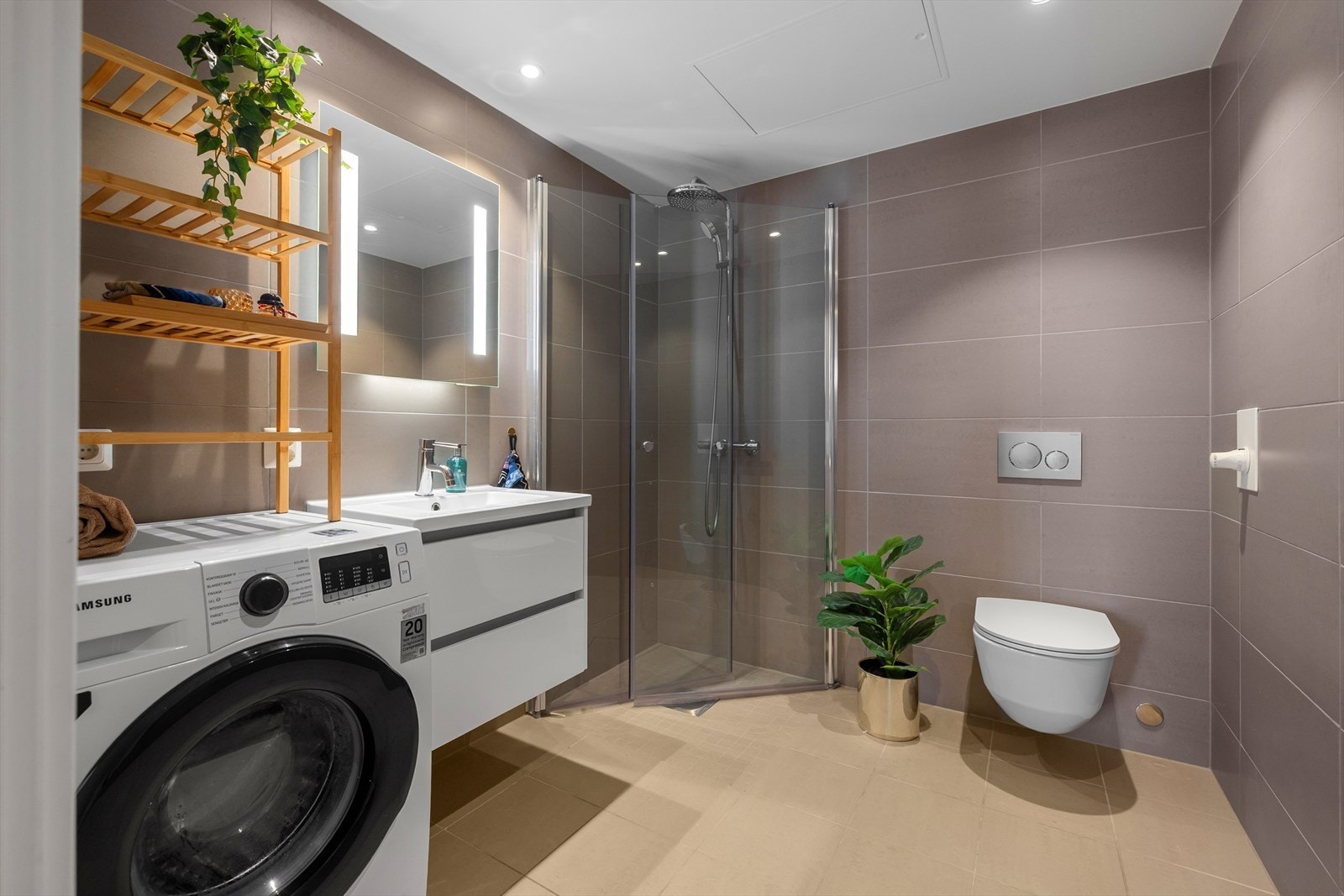 Stilrent baderom med klassisk innredning bestående av lyse kvadratiske fliser på gulv, med en noe mørkere tone på vegger. Det er montert downlights i himling, og speil med lys over servant. Galleribilde