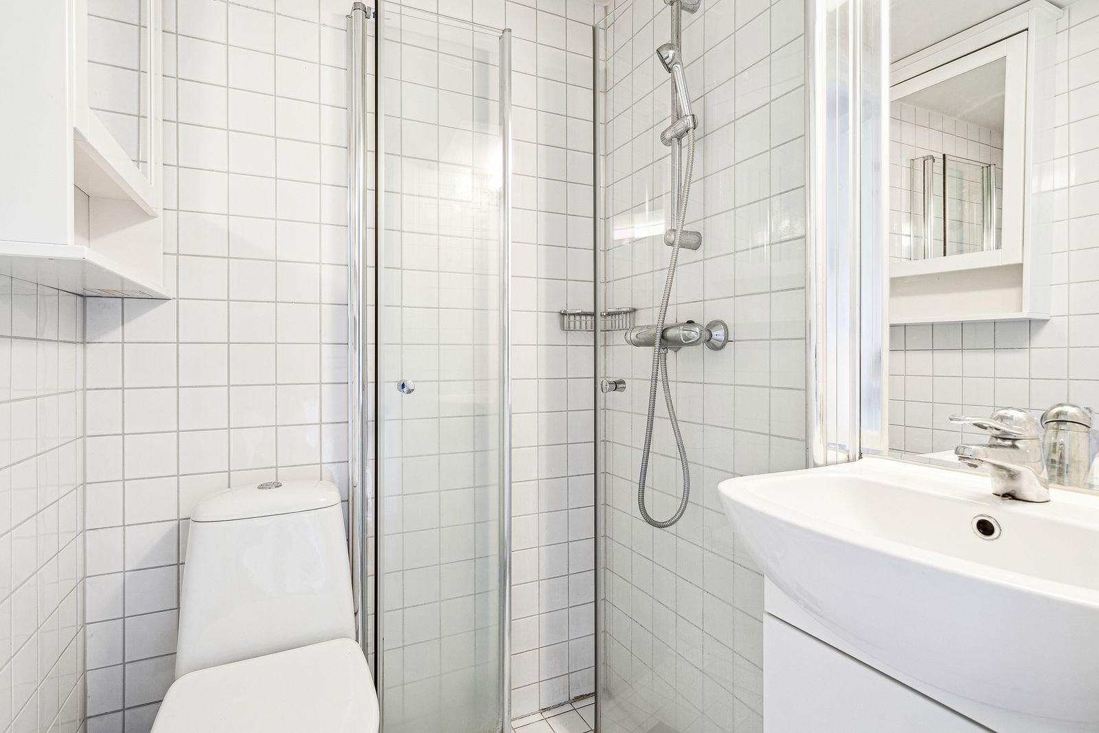 Lyst og flislagt bad med dusj, toalett, speil og vask med underskap. Galleribilde