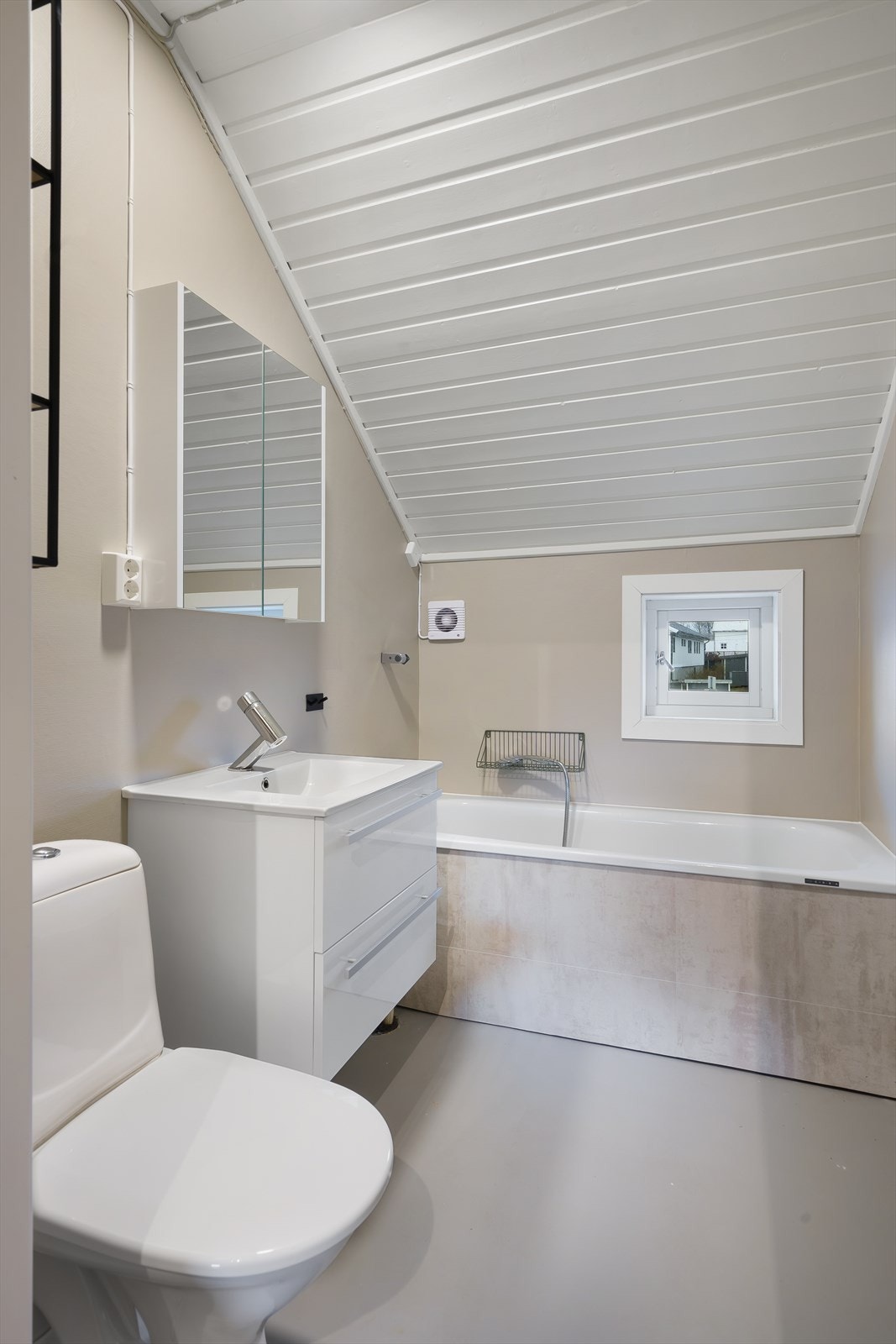 Badet er innredet med et toalett, badekar, en vask med underskap, overskap med speil og belysning. Galleribilde