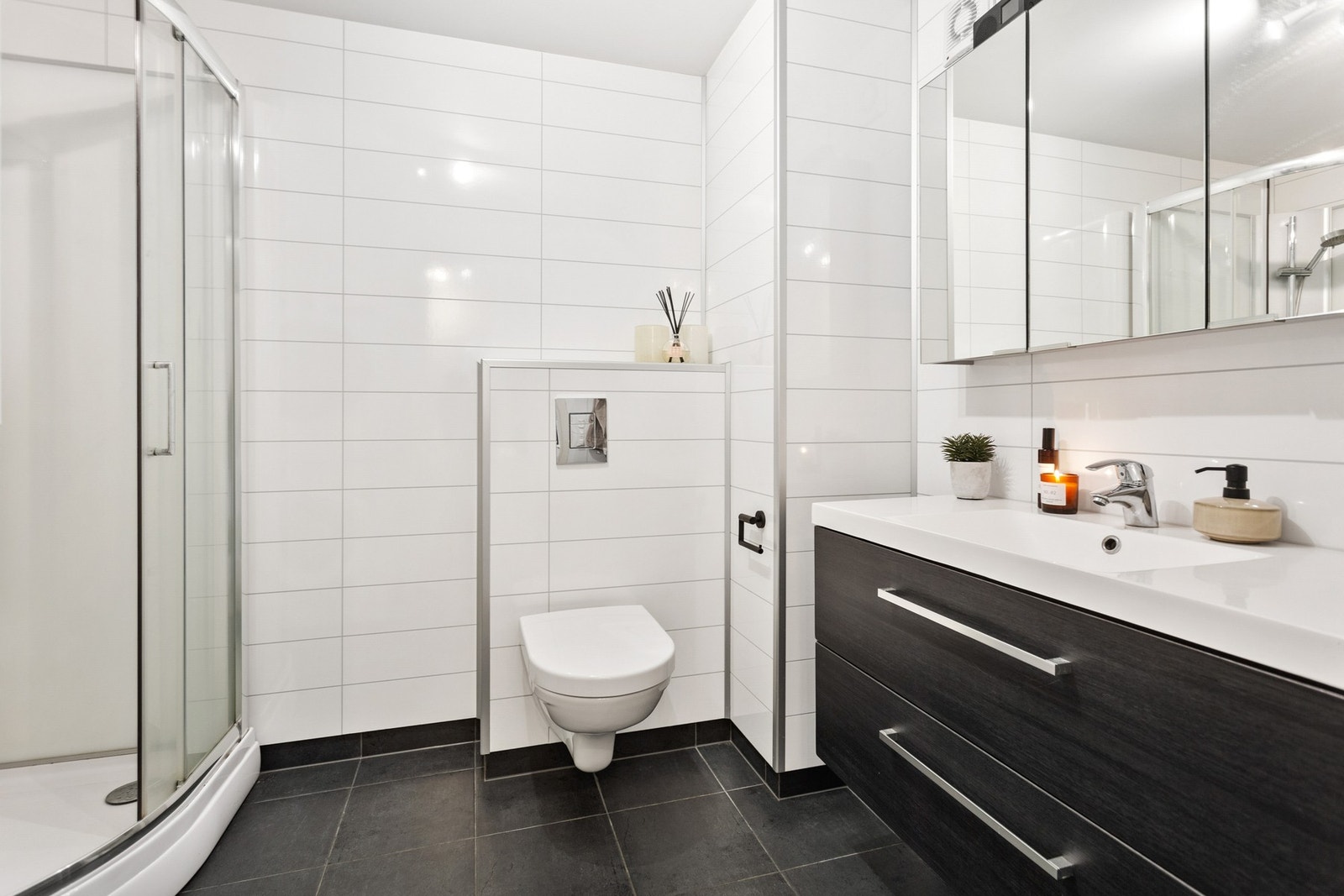Badet er flislagt og har vegghengt toalett, dusjkabinett og en romslig baderomsinnredning. Galleribilde
