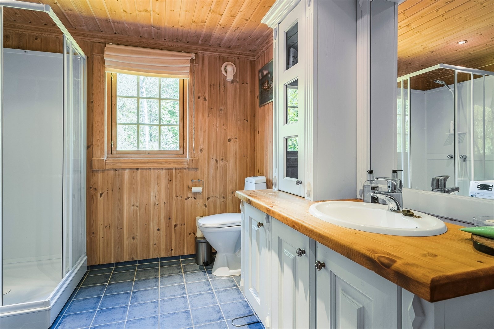 Fritidsboligen har to komplette bad - et i hver etasje. Baderommet i første etasje har flislagt gulv med varmekabler, og er innredet med dusjkabinett, servant nedfelt i romslig innredning med overskap, belyst speil og frittstående toalett. Galleribilde