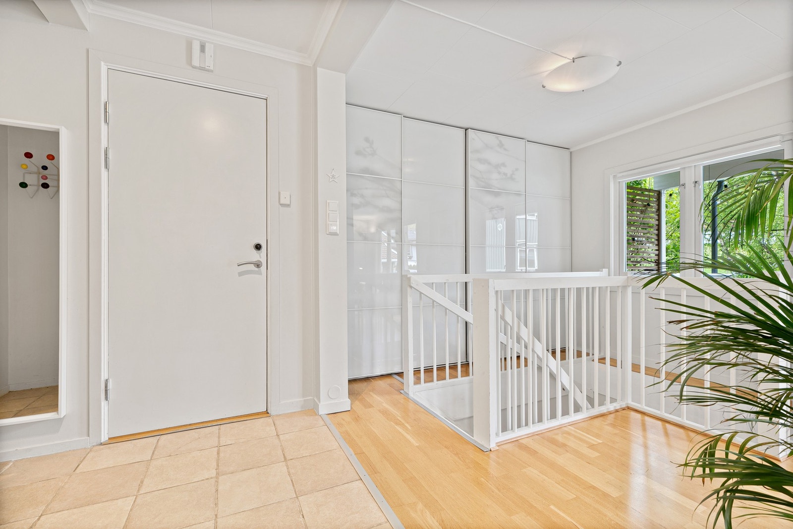 Entréen har flislagt gulv og en romslig stedtilpasset skyvedørsgarderobe med hvite fronter Galleribilde