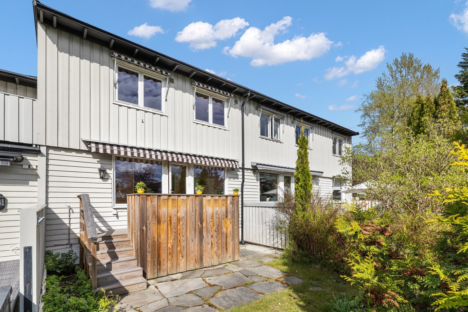 Mot syd har stuen utgang til en balkong med dekke av terrassebord, rekkverk i tre, markise og trapp ned til en hageflekk. Galleribilde