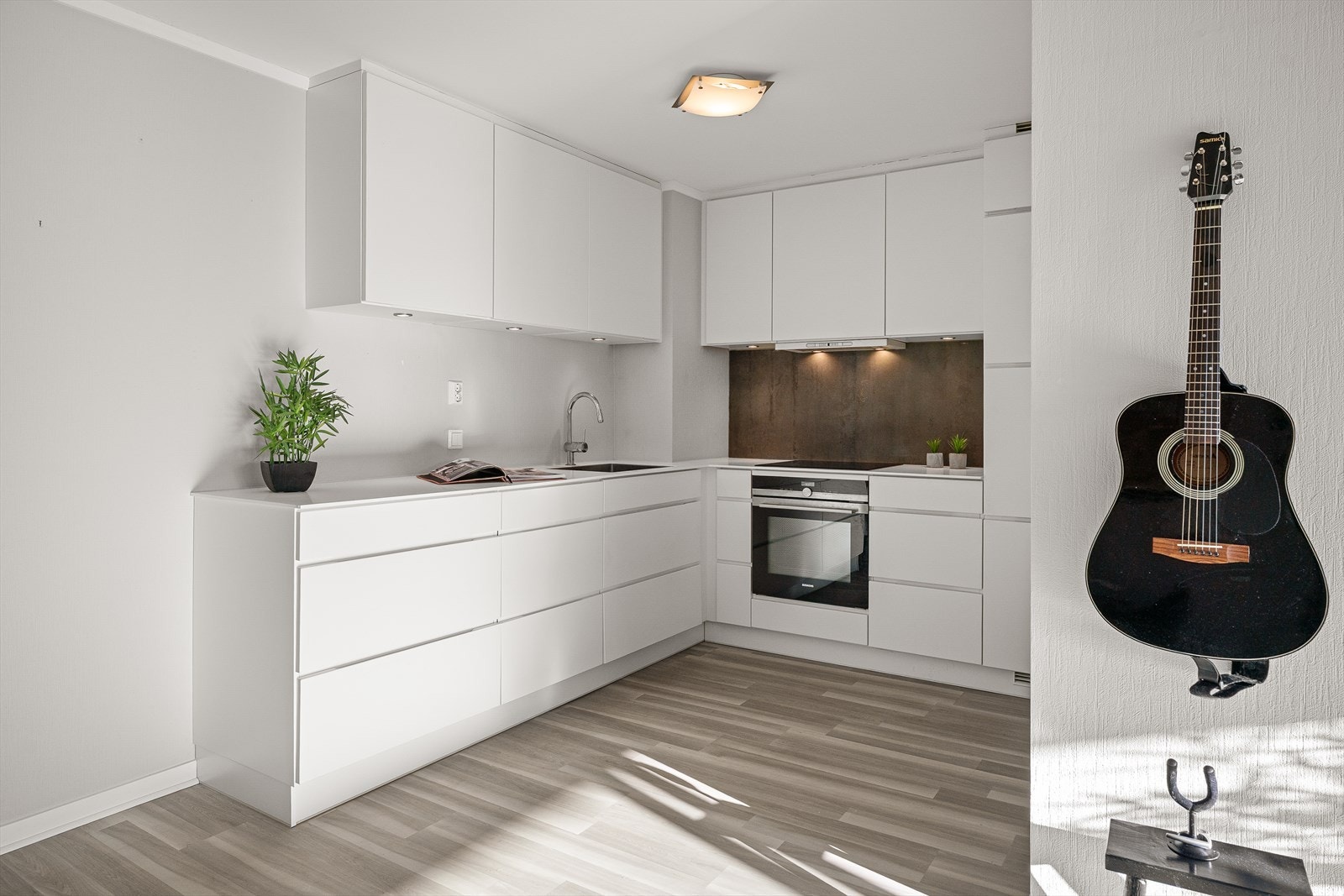 Innredningen består av hvite, glatte fronter, grå sprutplate over koketopp og benkeplate i hvit kompositt med stor stålkum. Galleribilde