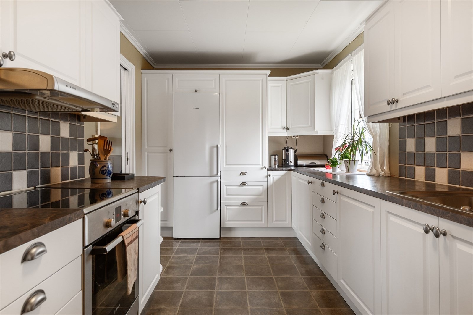 Kjøkkenet er innredet med laminerte skrog, profilerte fronter og laminert benkeplate med kjøkkenkum, og med plass til frittstående komfyr, oppvaskmaskin og kjøleskap. Galleribilde