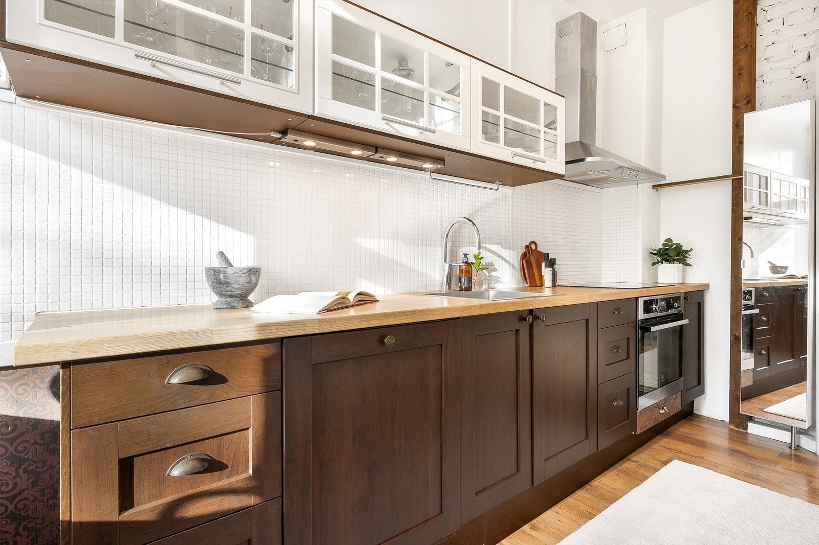 Innredning med profilerte finerte/malte fronter, laminat benkeplate med fliser på bakvegg, rustfri oppvaskkum, ventilator med kullfilter og innfelte hvitevarer som stekeovn, platetopp, kjøl/frys og oppvaskmaskin Galleribilde