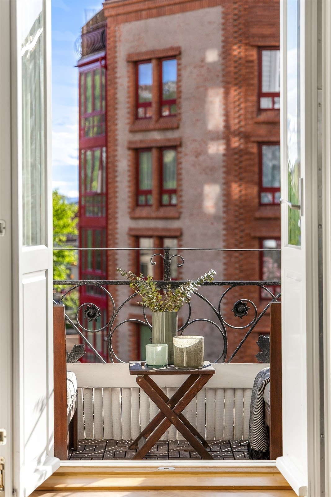 Balkongen har en tofløyd dør, trefliser på gulvet og et rekkverk av lakkert smijern Galleribilde