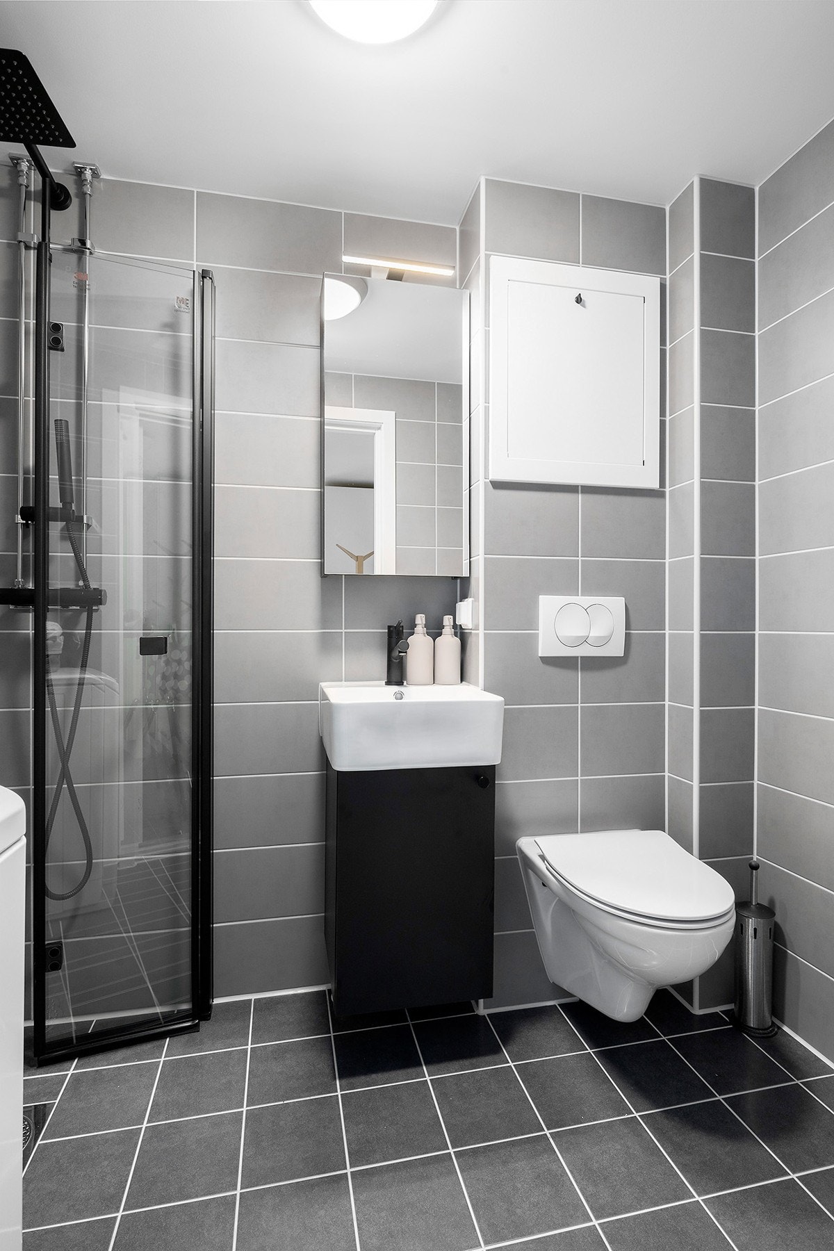 Meget delikat bad i tidsriktige grå toner med servant m/underskap, dusjplass med innsvingbare dører av glass og vegghengt wc. Det er opplegg for vaskemaskin. Galleribilde