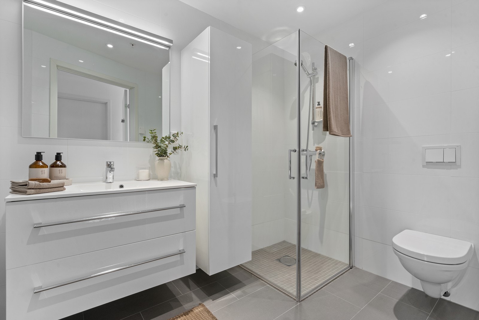 Lekkert helfliset bad med dusjhjørne, vegghengt toalett, vask i seksjon, skap. Vannbåren gulvvarme. Galleribilde