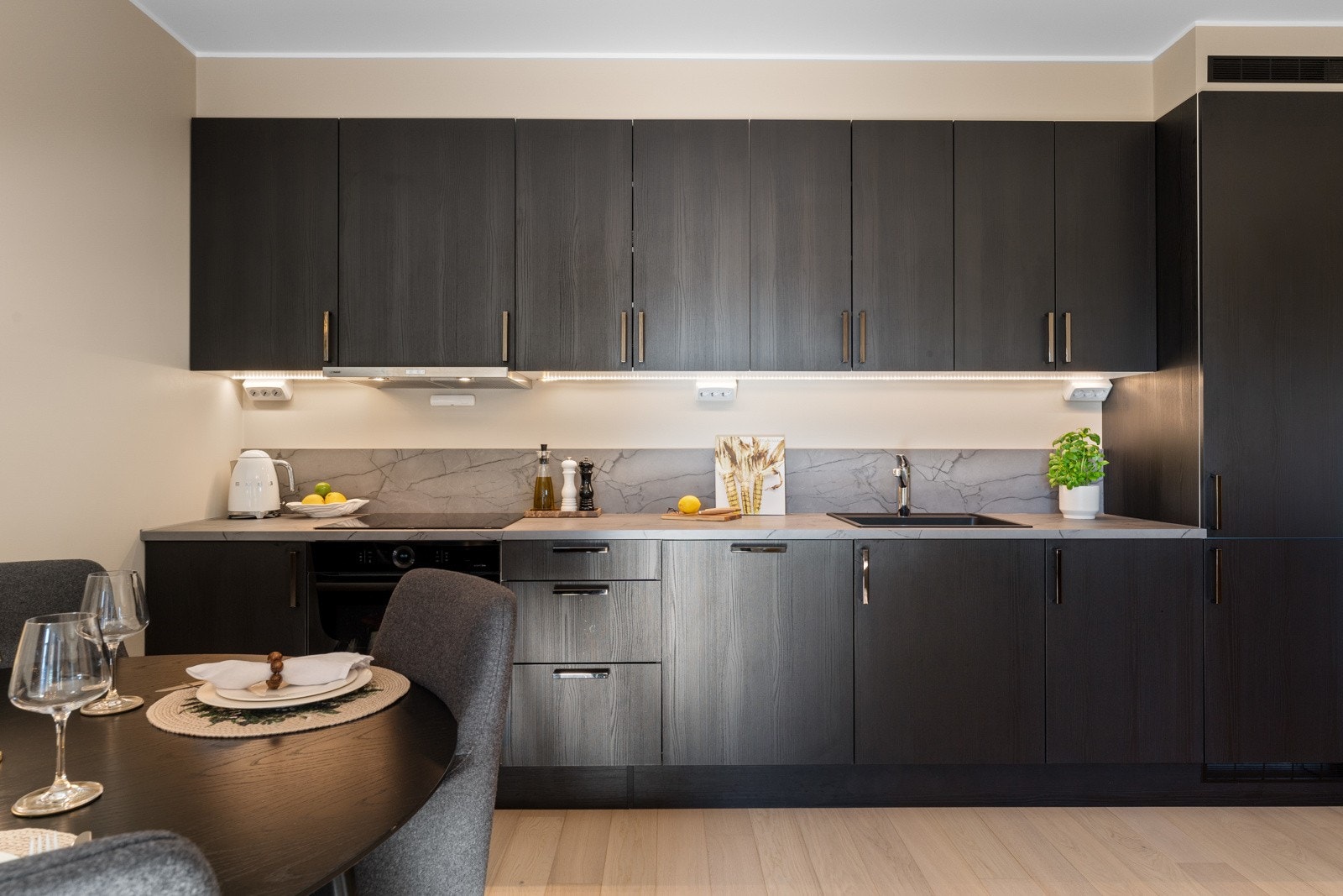 Kjøkkeninnredningen er rålekker med mørke strukturerte fronter og laminert benkeplate i stenmønster med oppbrett i sprutsone og vegg. Galleribilde