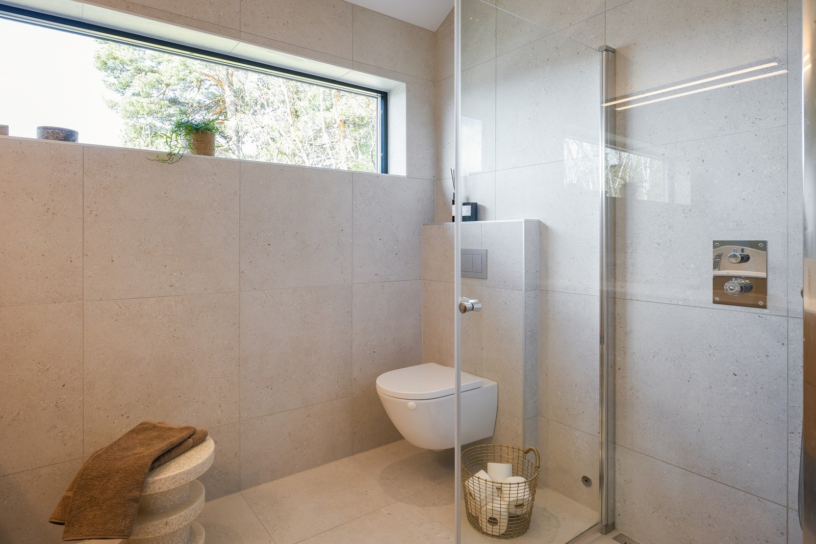 Badet er utstyrt med gulvvarme, vegghengt toalett og dusjhjørne. Lekre detaljer med skjult dusjarmatur, nisjehylle for dusjartikler, og avlang dusjrist over sluk. Galleribilde