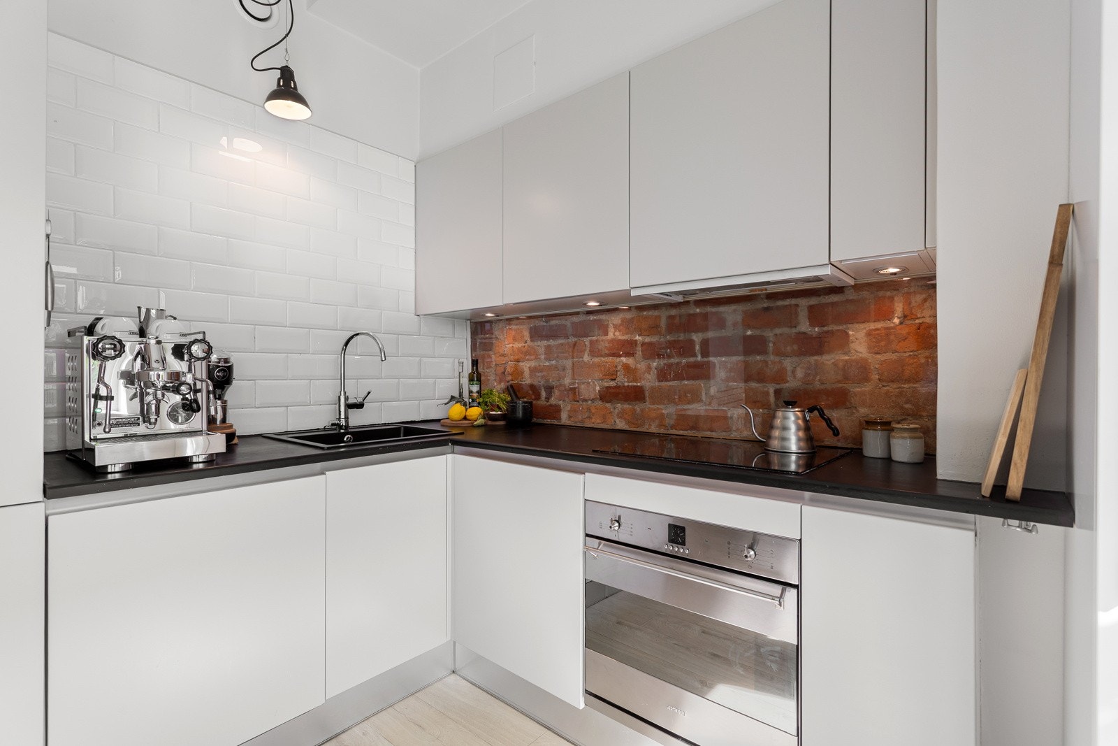 Lekkert kjøkken med lyse glatte flater, heltre kjøkkenbenk ognydelig eksponert teglsteinsvegg. Galleribilde