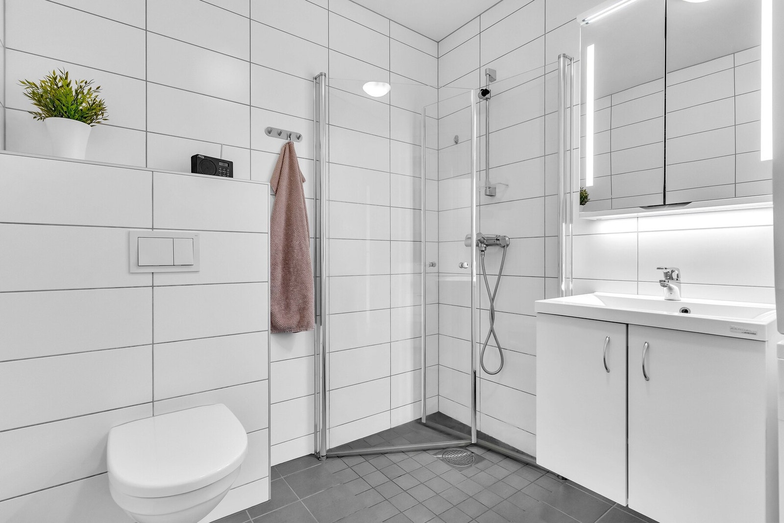 Badet er holdt i lyse, nøytrale farger og innredningen består av heldekkende servant på underskap og speilskap med belysning Galleribilde