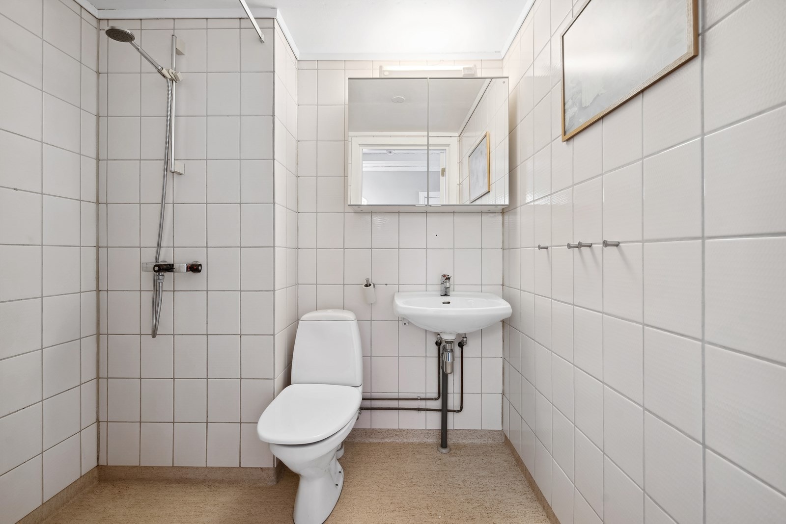 Badet er innredet med en enkel servant, speilskap med overliggende belysning, dusjnisje med forheng og et gulvstående toalett. Galleribilde