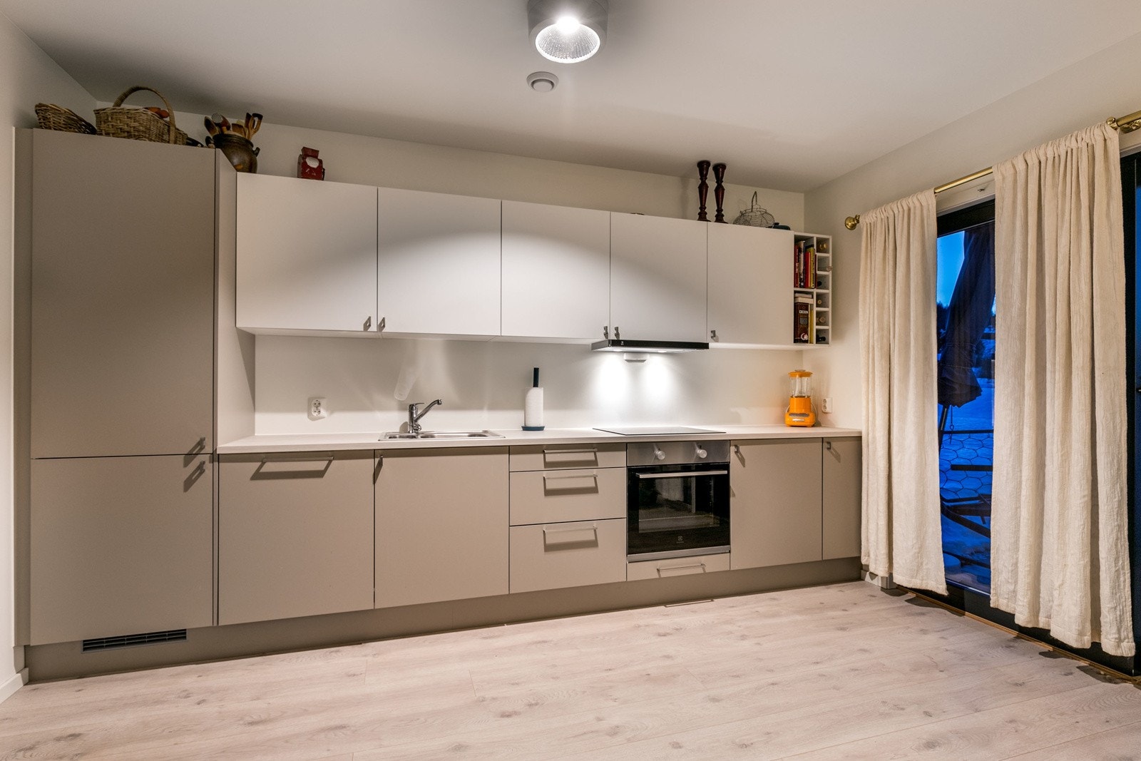 Stilrent kjøkken fra byggeår. Innredningen består hvite og brune fronter med slett utførelse. Laminat benkeplate med nedfelt kum i rustfritt stål. Galleribilde