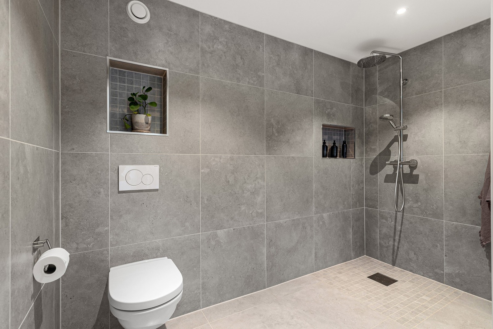 Badet er utstyrt med veggmontert toalett, dusjhjørne og servant i skap. Legg merke til veggnisjeene med plass til oppbevaring. Galleribilde