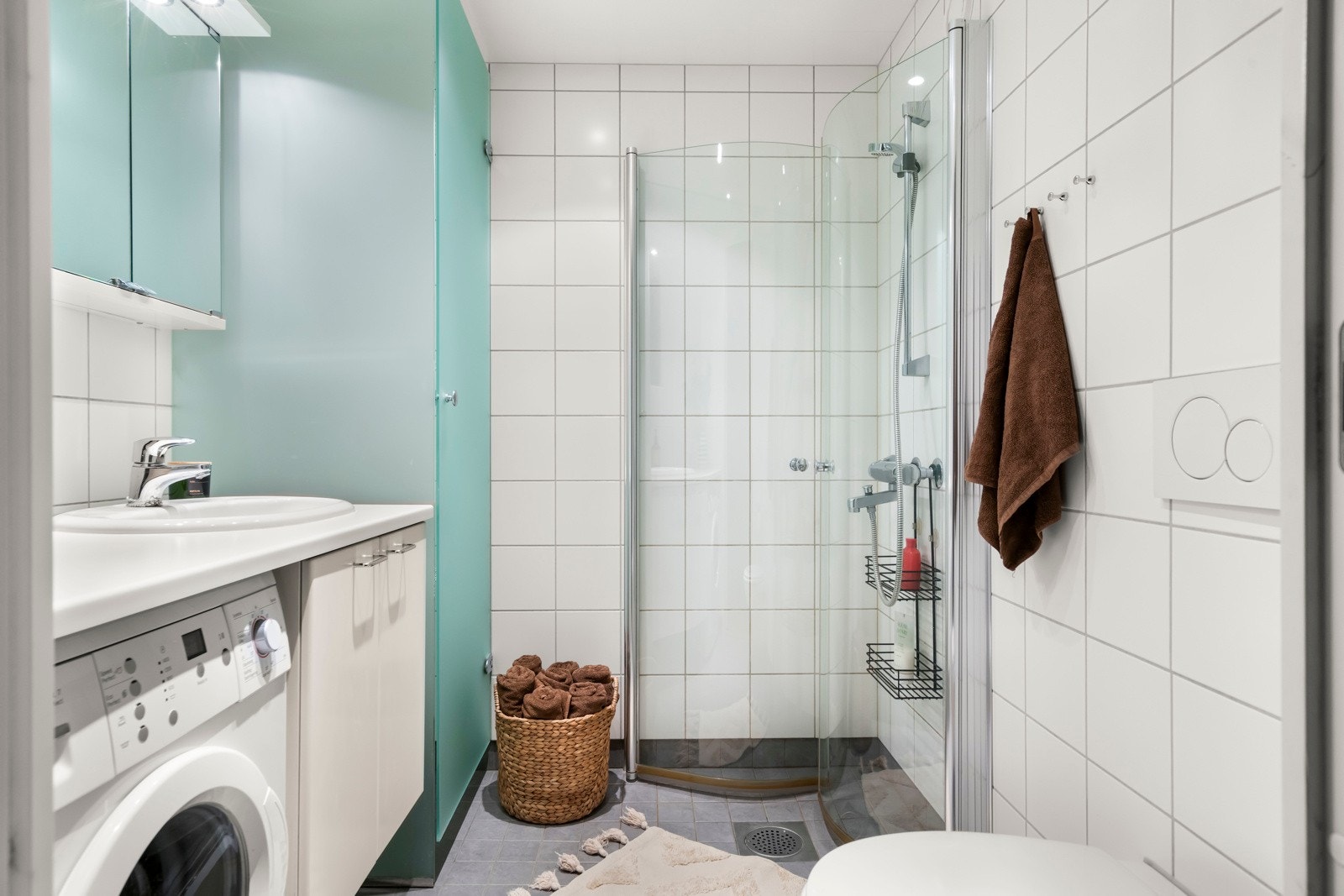 Romslig baderom med lyse flis- og materialvalg. Opplegg for vaskemaskin og tørkeskap for å nevne noe. Galleribilde