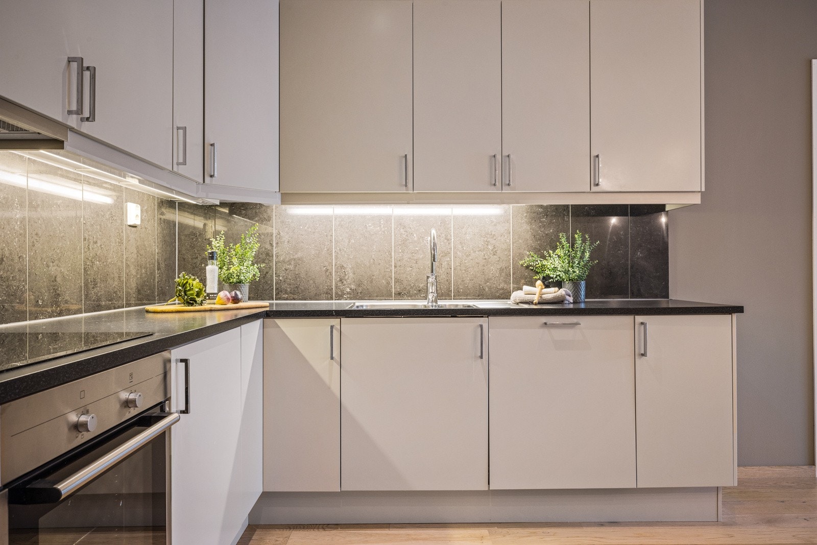 - Pent kjøkken med lyse slette fronter. Integrert induksjonsplatetopp, stekeovn, oppvaskmaskin og kombinert kjøl- og fryseskap - Galleribilde