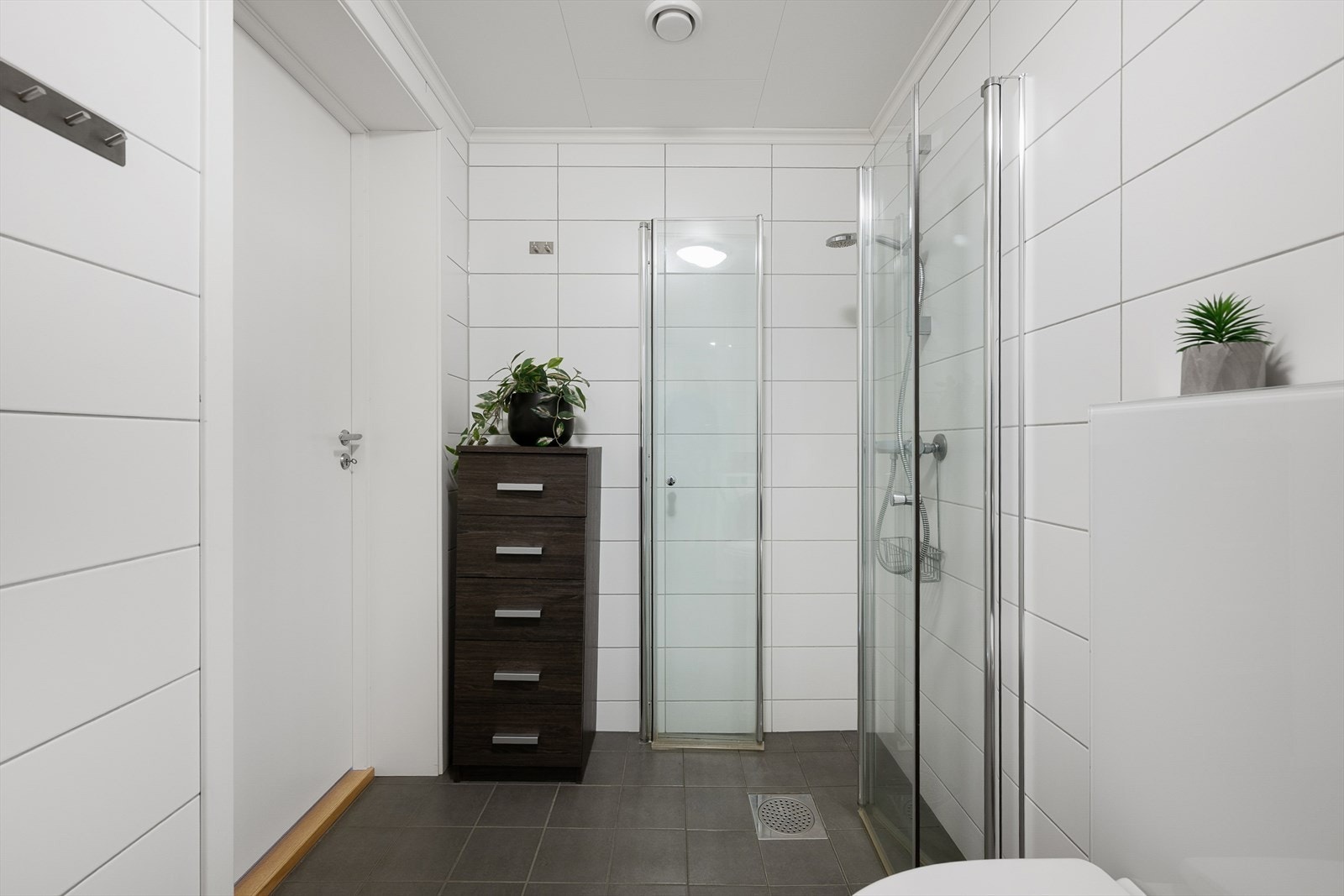 Badet har vegghengt toalett, opplegg til vaskemaskin, dusjhjørne med glassdører, servant med speil og mekanisk avtrekk. Galleribilde