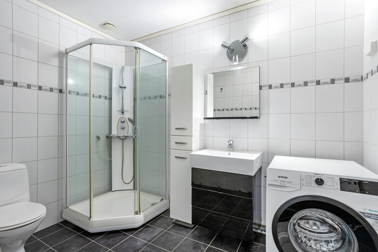 Badet har flislagte vegger og gulv, med dusjkabinett og opplegg til vaskemaskin. Galleribilde