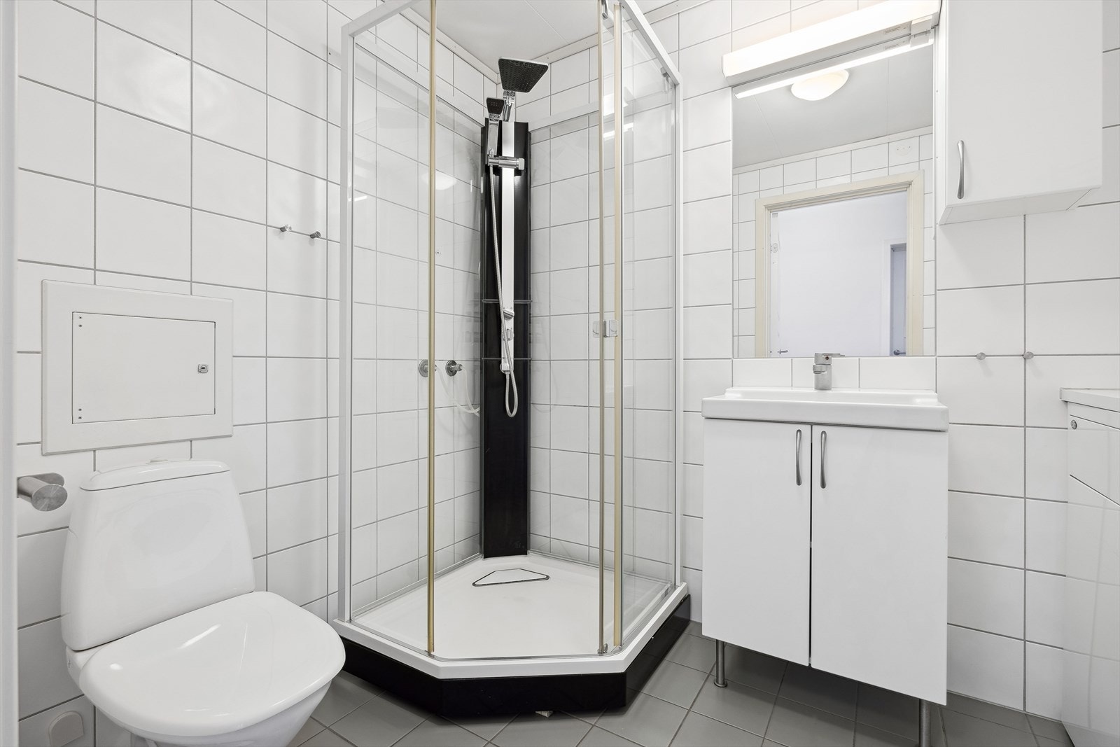 Badet er bestående av baderomsinnredning med servant og ett-greps blandebatteri, speil, lys, dusjkabinett og gulvstående toalett. Galleribilde