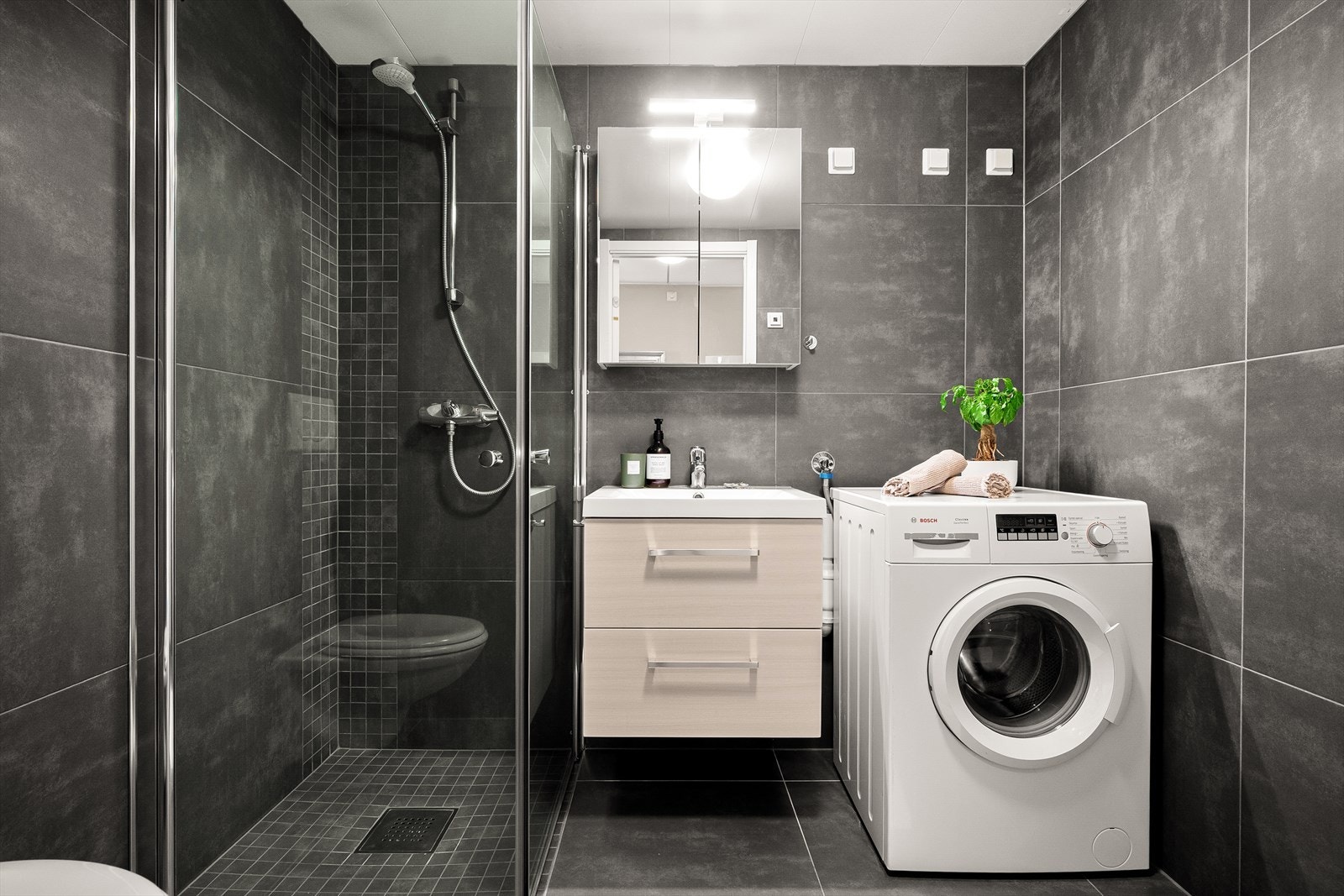 Delikat bad med hjørnedusj, veggmontert toalett, servant med skuffer og speilskap. Galleribilde