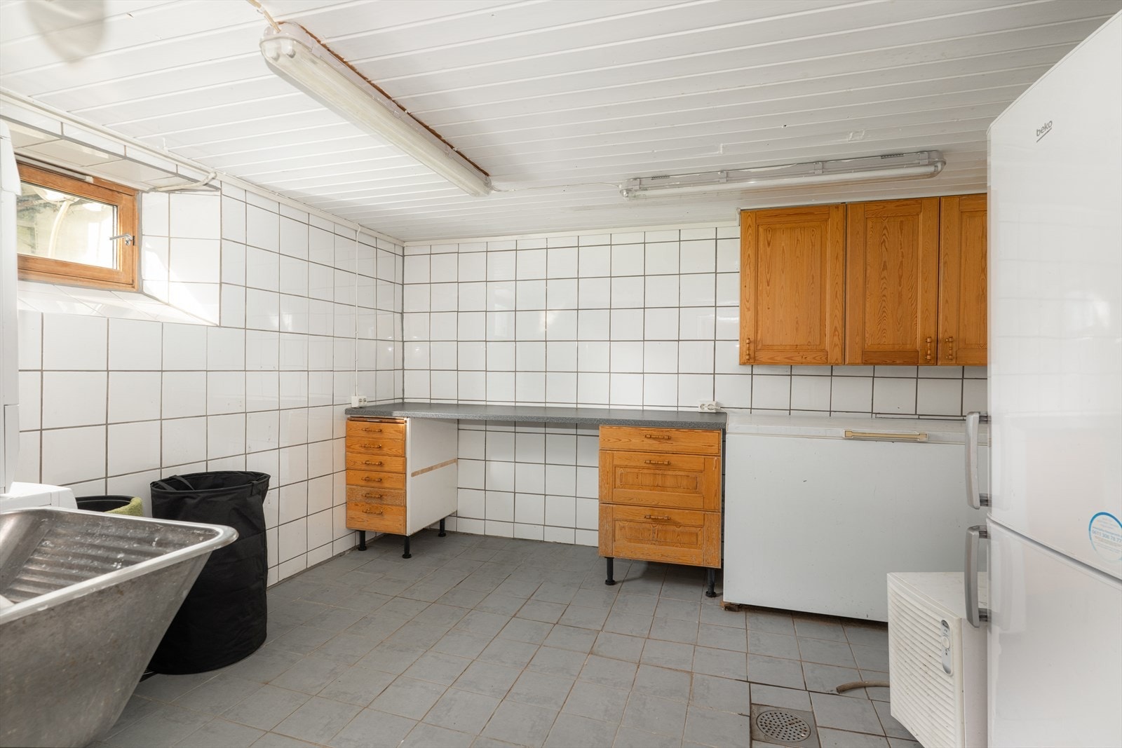 Flislagt vaskerom som er innredet med utslagskum av stål og opplegg for vaskemaskin. Galleribilde