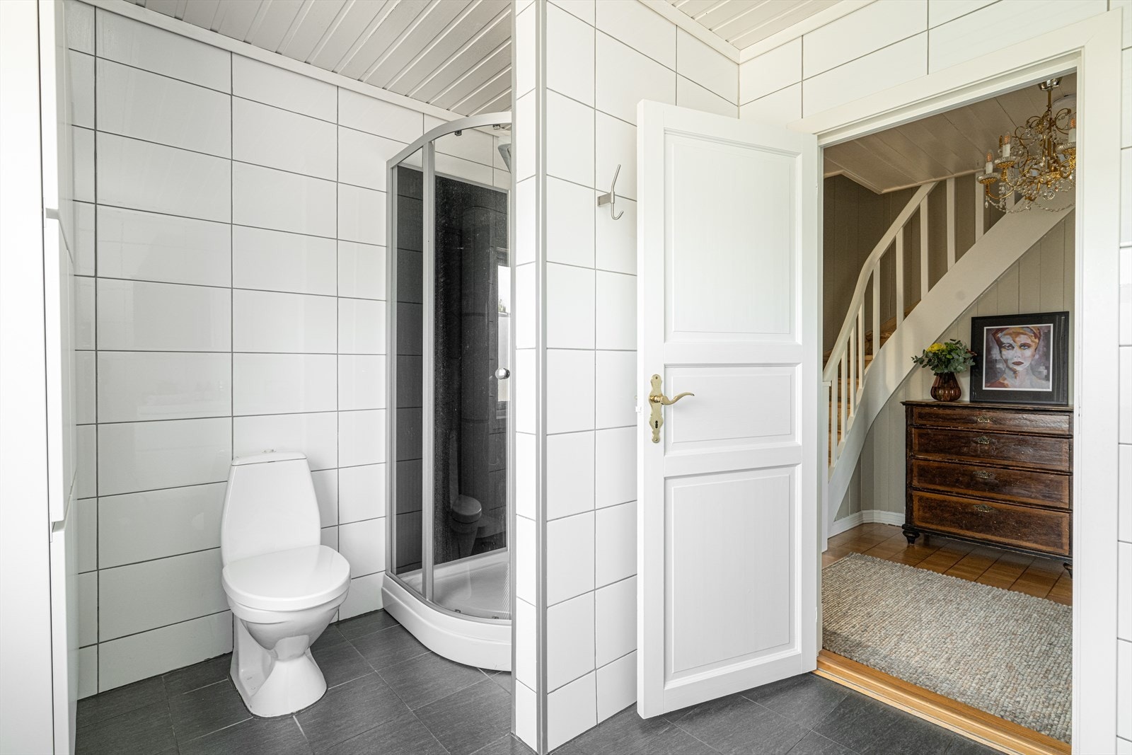 Badet er innredet med toalett, dusjkabinett og servantinnredning med underskuffer, overskap med speildører. Det er elektrisk styrt vifte på vegg. Galleribilde